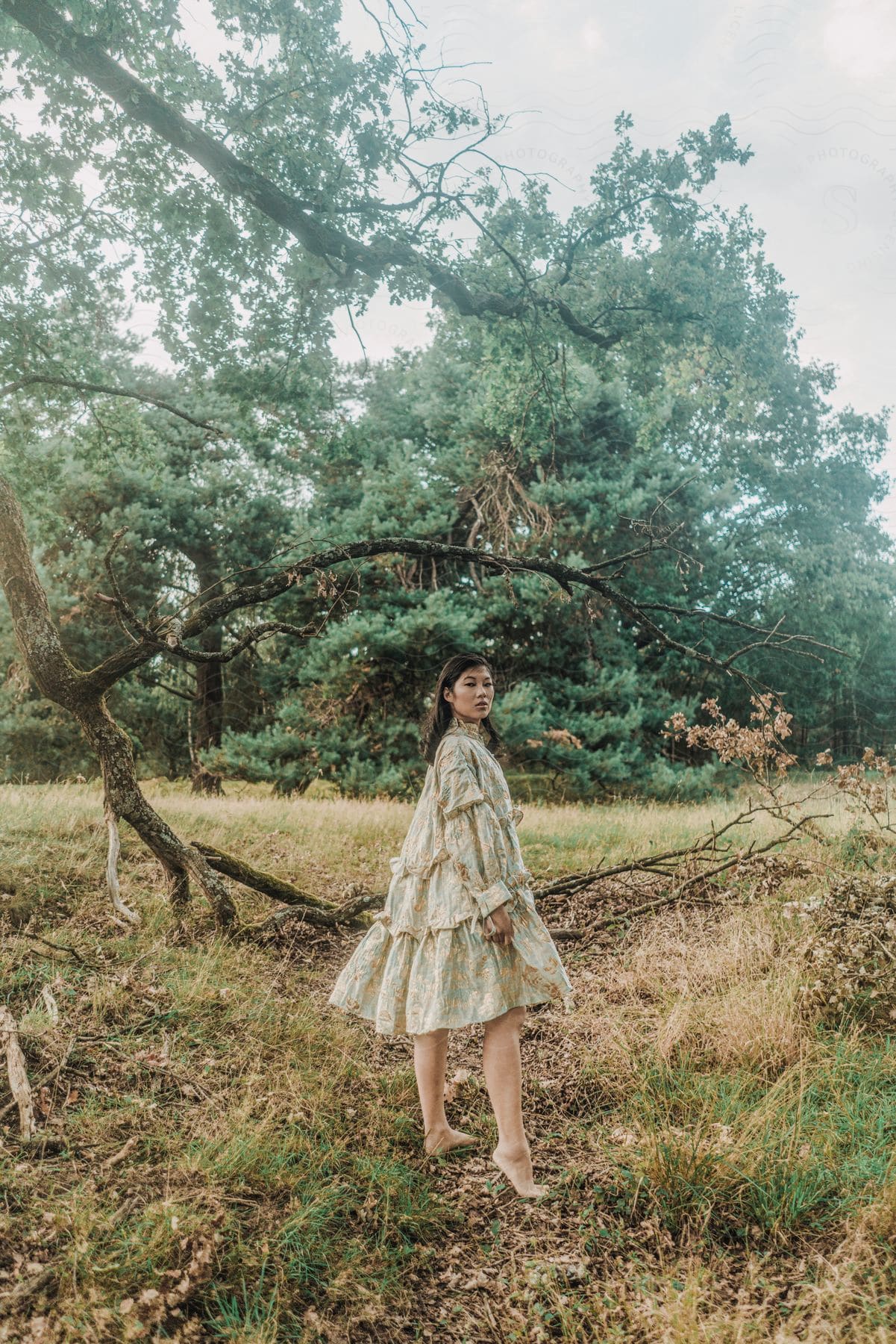 Woman stands outdoors looking to the side near a tree.