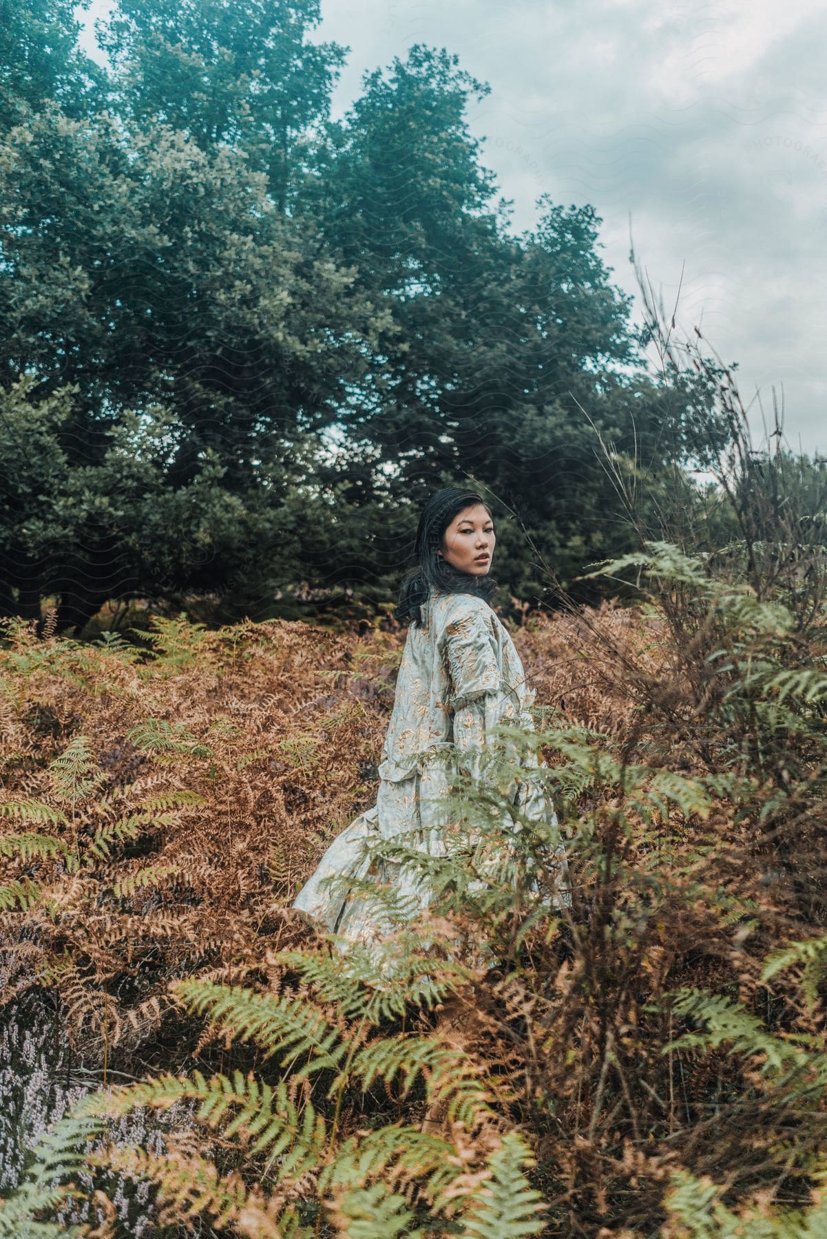 Woman standing in a field of ferns in nature in the middle of the day as she looks back over her shoulder.