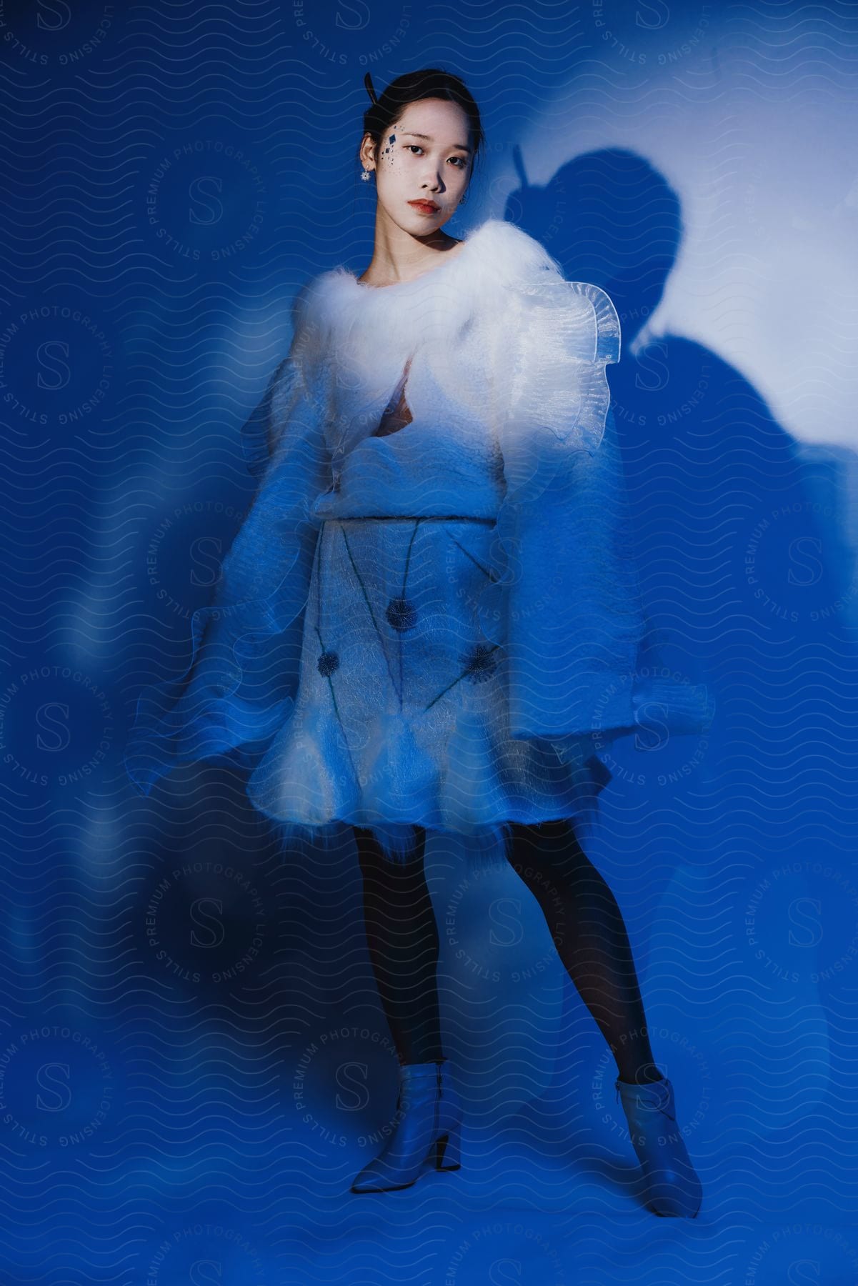 A woman stands near a wall as she models winter fashion long sleeves and tights with a skirt and boots