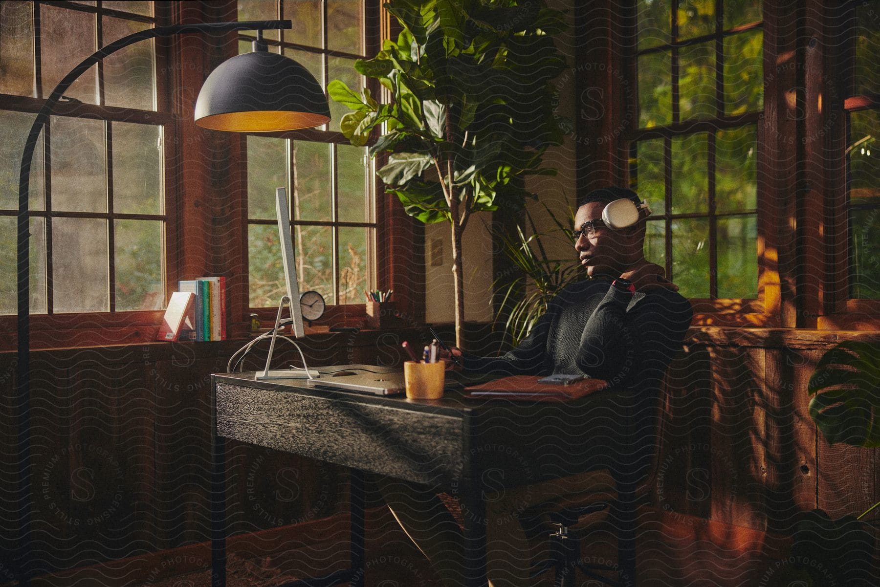 A black man sits at a rustic desk in a home office and stares at a computer monitor.