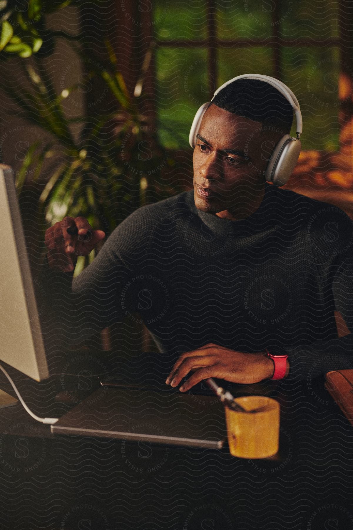 A man wearing headphones is sitting at a desk as he looks at a computer monitor