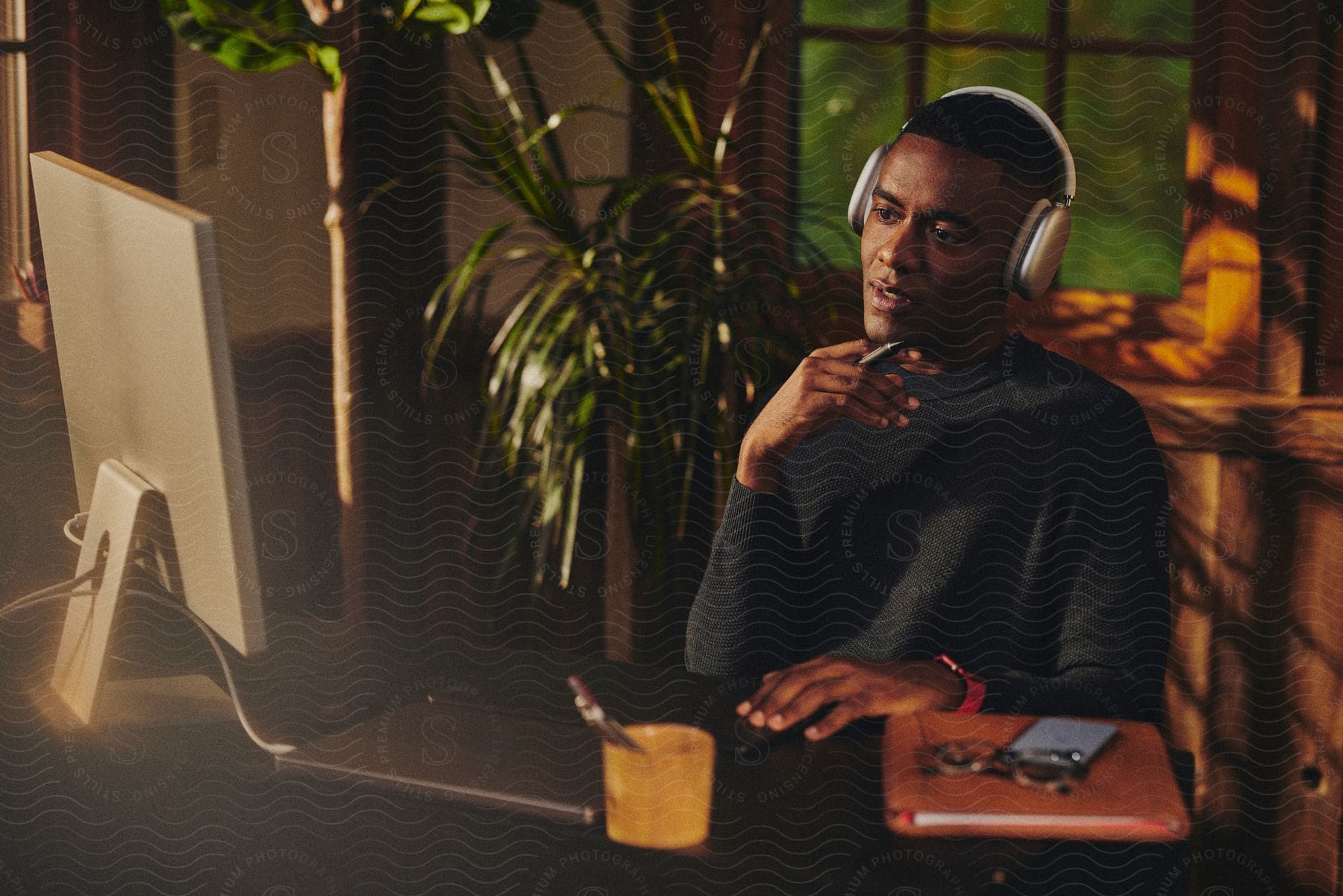 A man sitting down at a desk with a computer while wearing headphones.