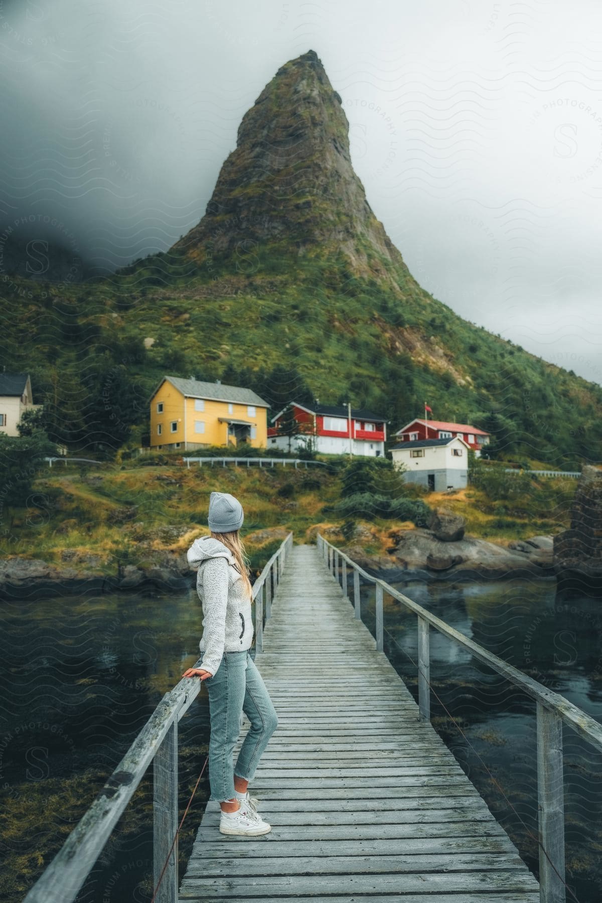 a woman stands on a bridge over a river near a mountains