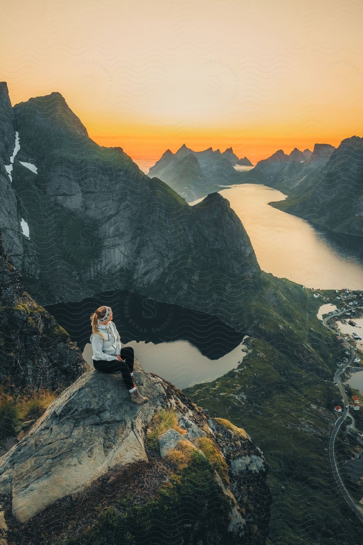 A woman sits high on a rocky peak overlooking mountainous rock formations in the water along the coast