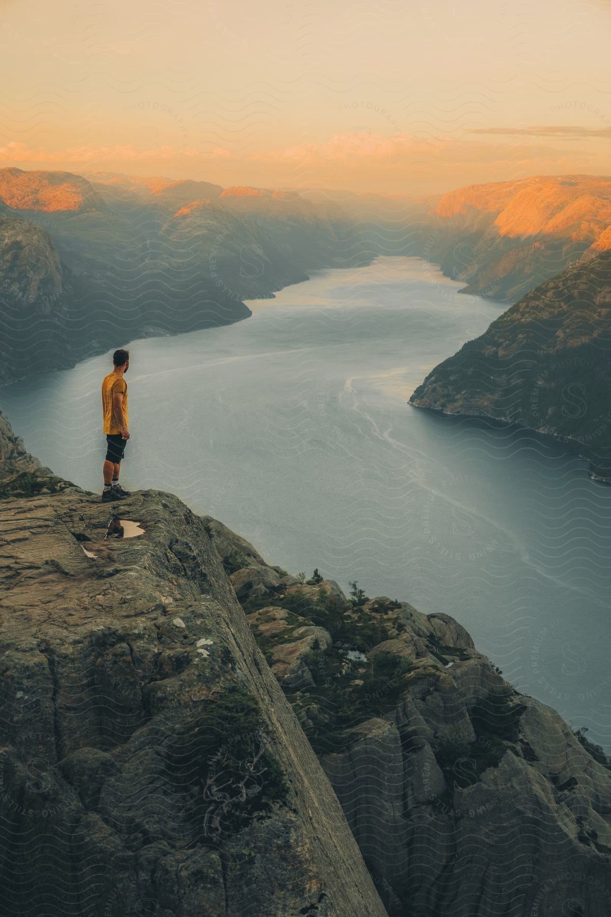 A man is standing on a mountain watching the sunset on the mountains in the distance.