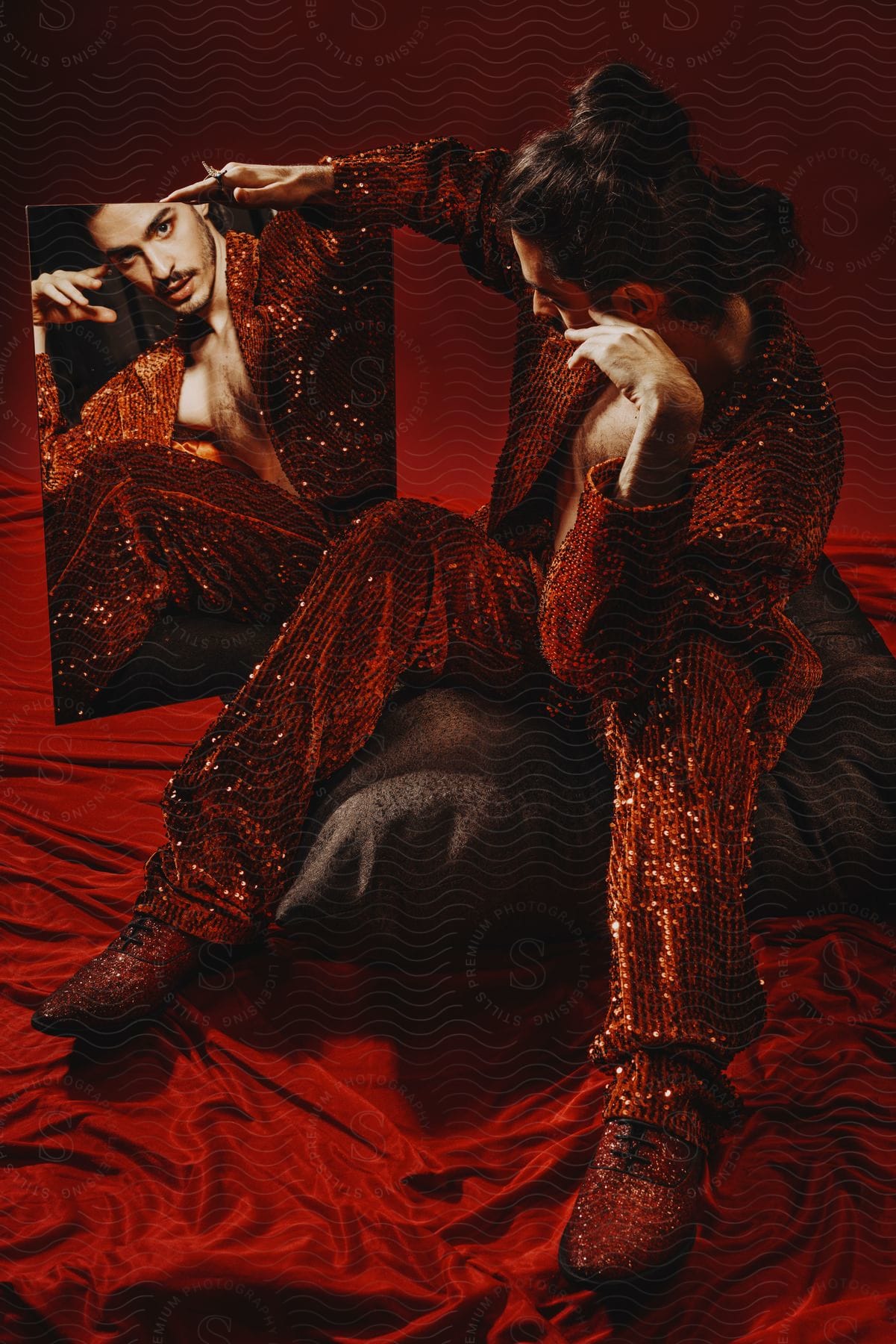 A male model dressed in sequin clothes admiring himself in a mirror.