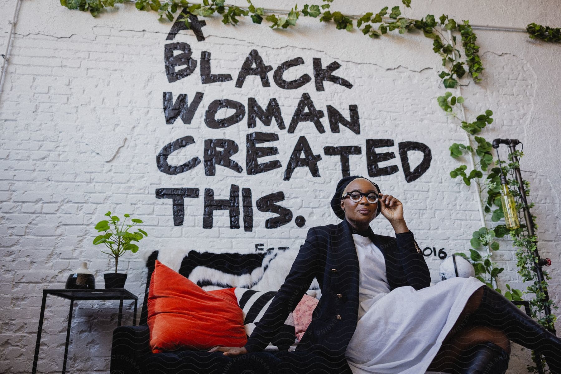 A black woman sits and poses in front of an inspirational message painted on the brick wall behind her.