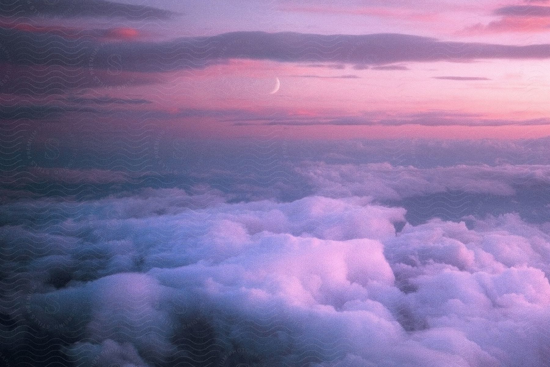 a crescent moon forms over fluffy clouds at dusk