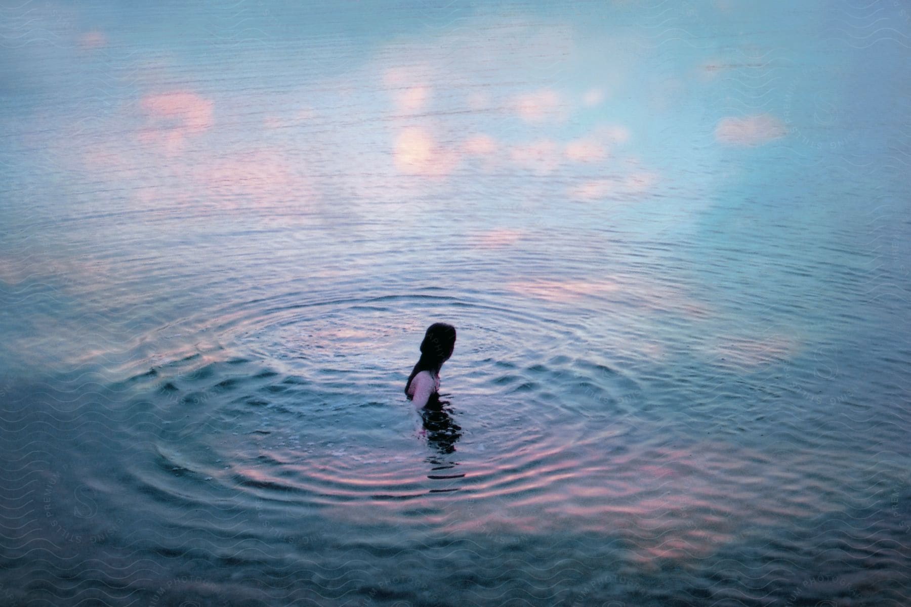 Someone is swimming in a body of water where the clouds are reflecting on the water.