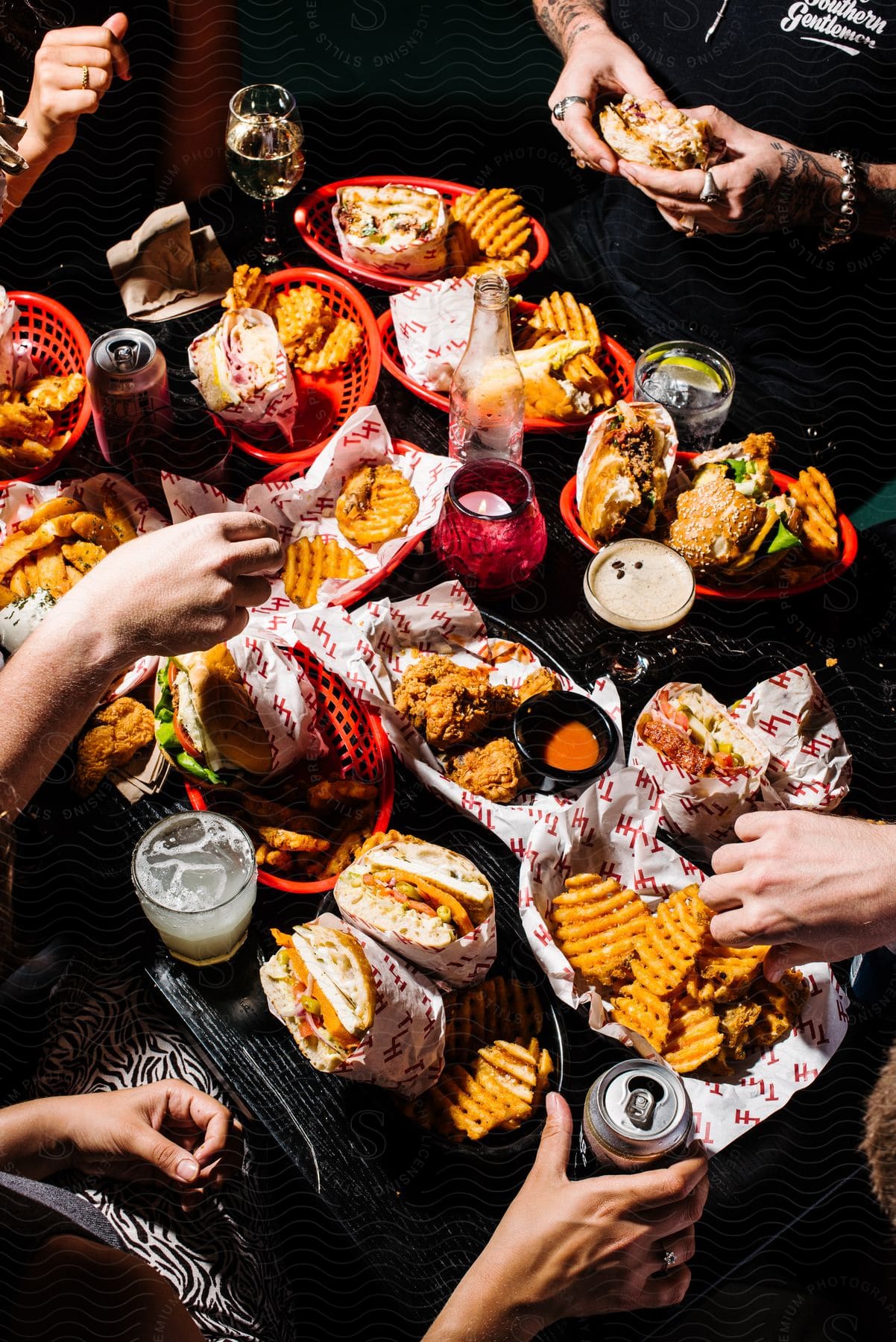 Baskets of food cover a table as people sit around with food in their hands as they eat