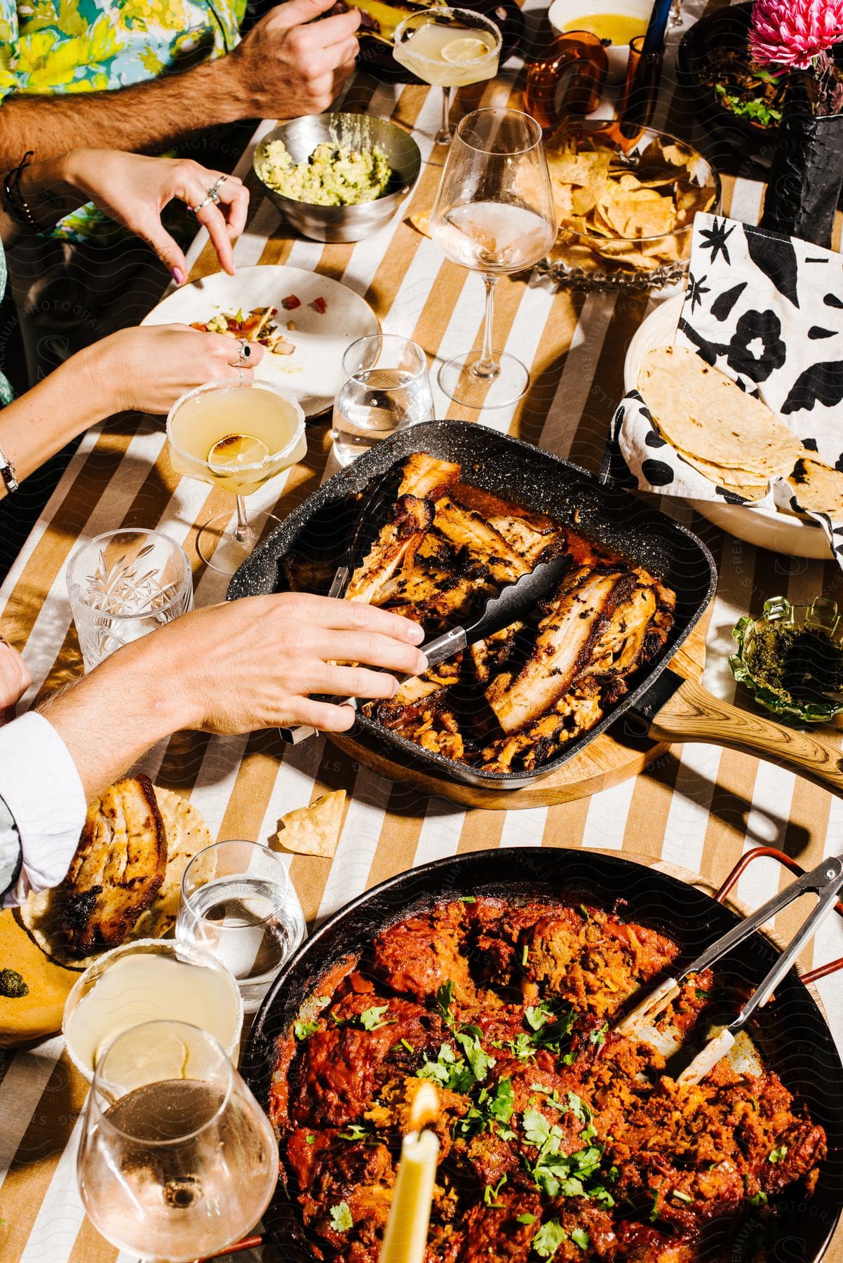 Hands at an outdoor table reaching for hot food and chips salsa and guacamole and margaritas