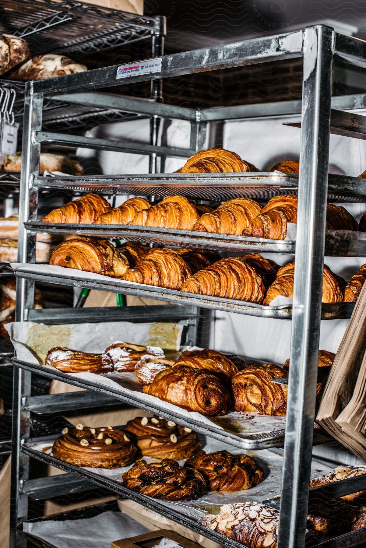 A bakery rack overflowing with breads, pastries, croissants, and almond-topped pastries.