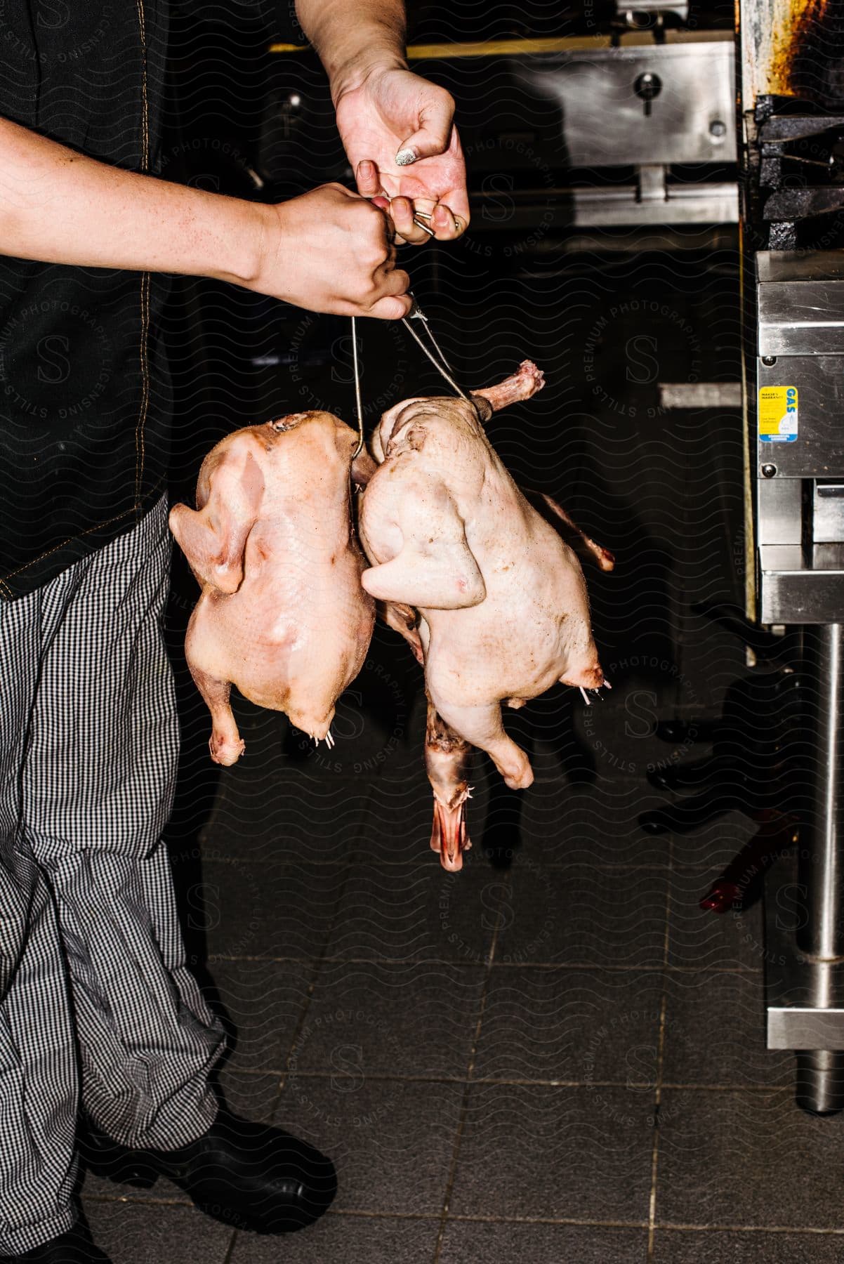 A man is standing in a kitchen holding chickens on hooks for the roaster