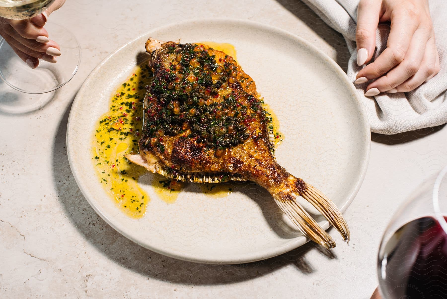 A woman's hands are on a table with a fish on a plate ready to eat