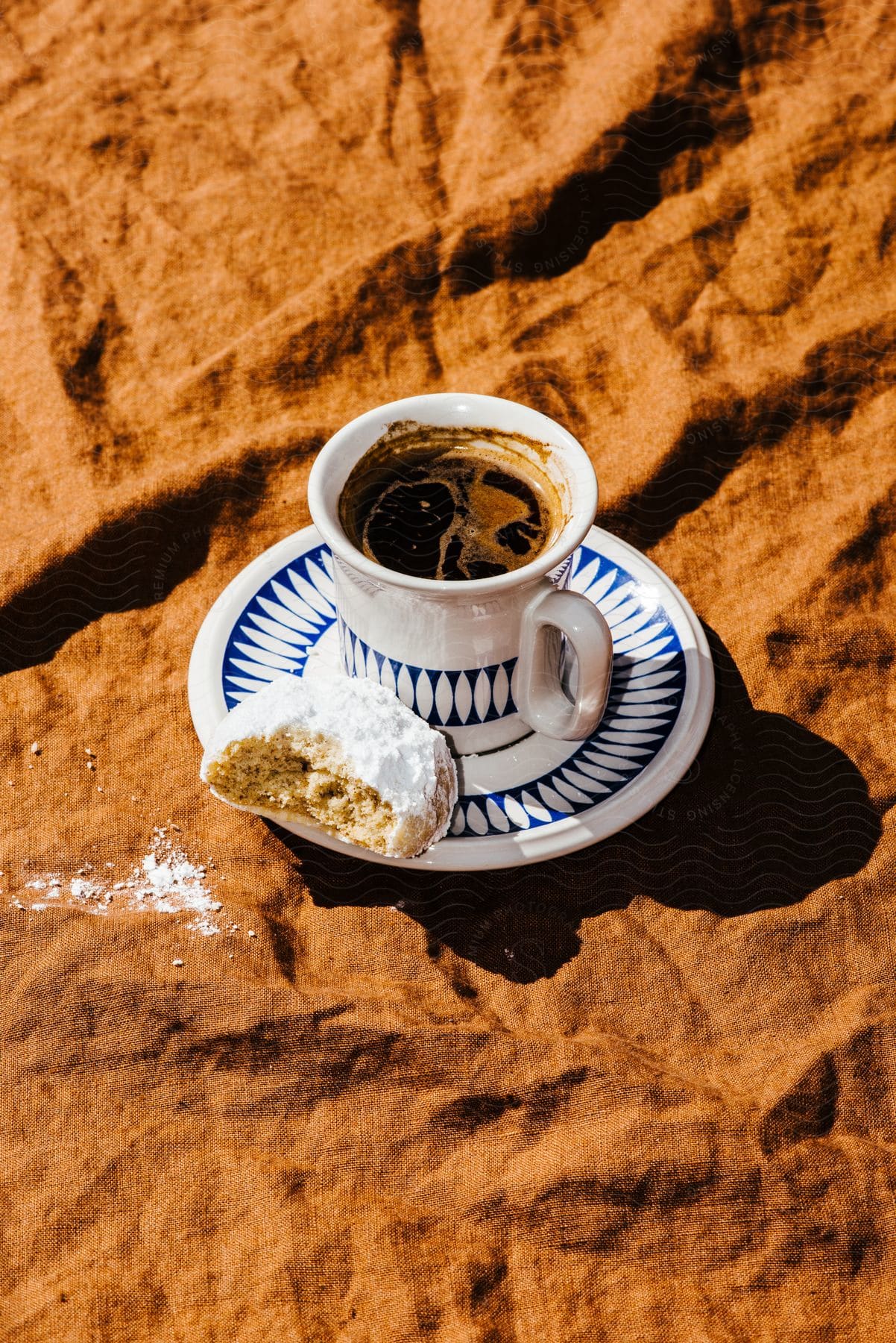 The sun shines upon a cup of coffee with a half eaten biscuit on the saucer