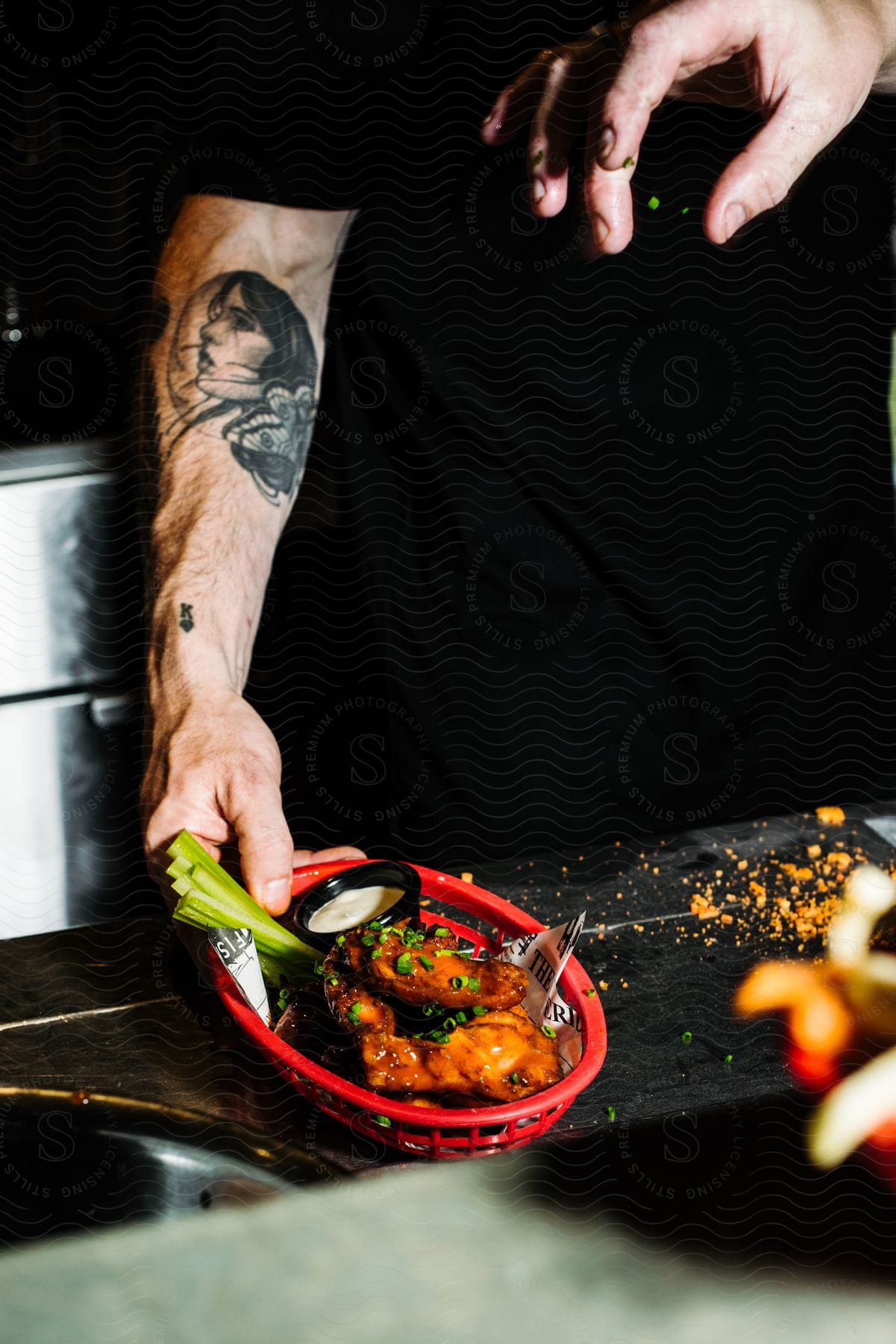 A man holds a basket of fried chicken with celery as another hand reaches down