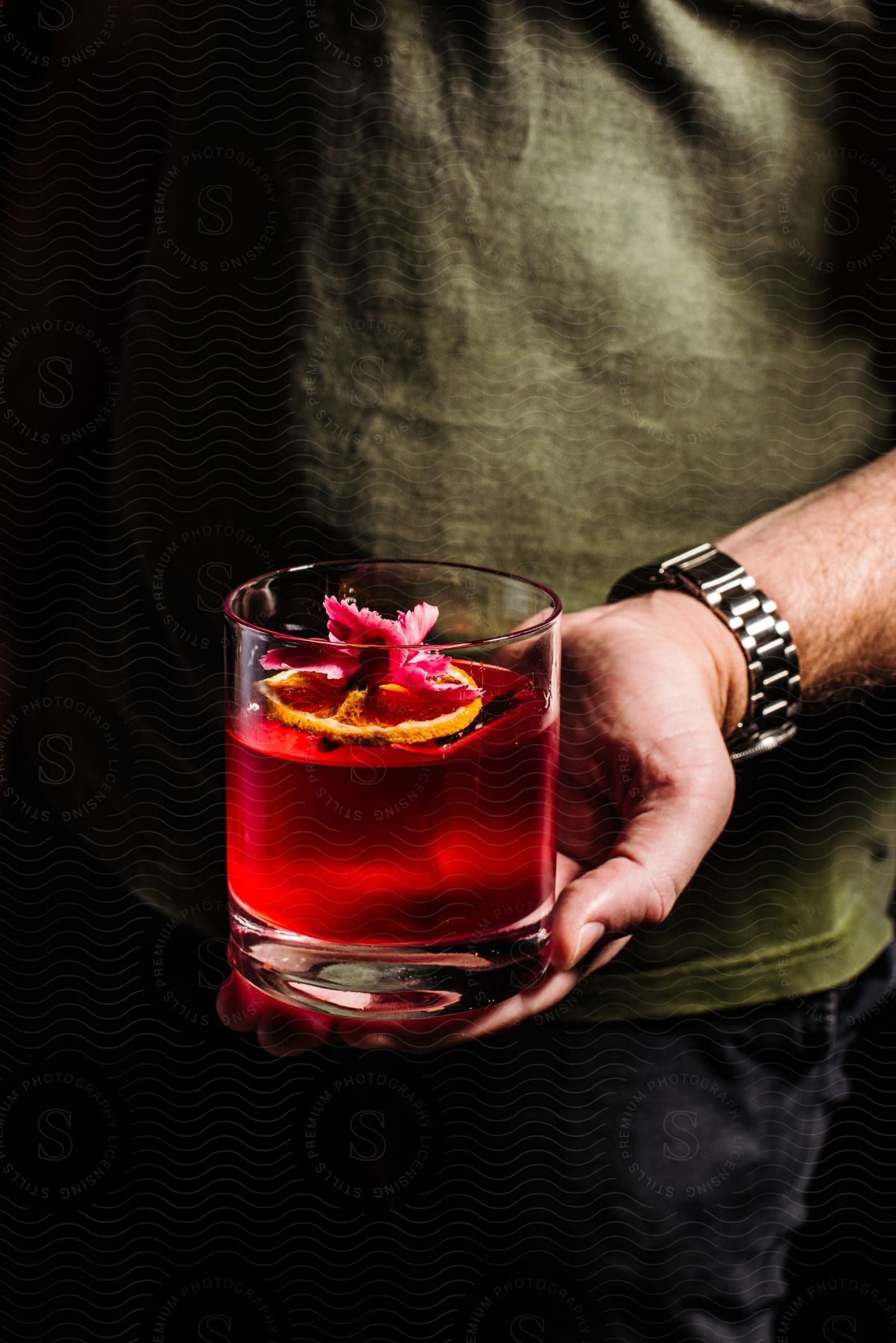 A man holds a drink with a slice of lemon floating on top