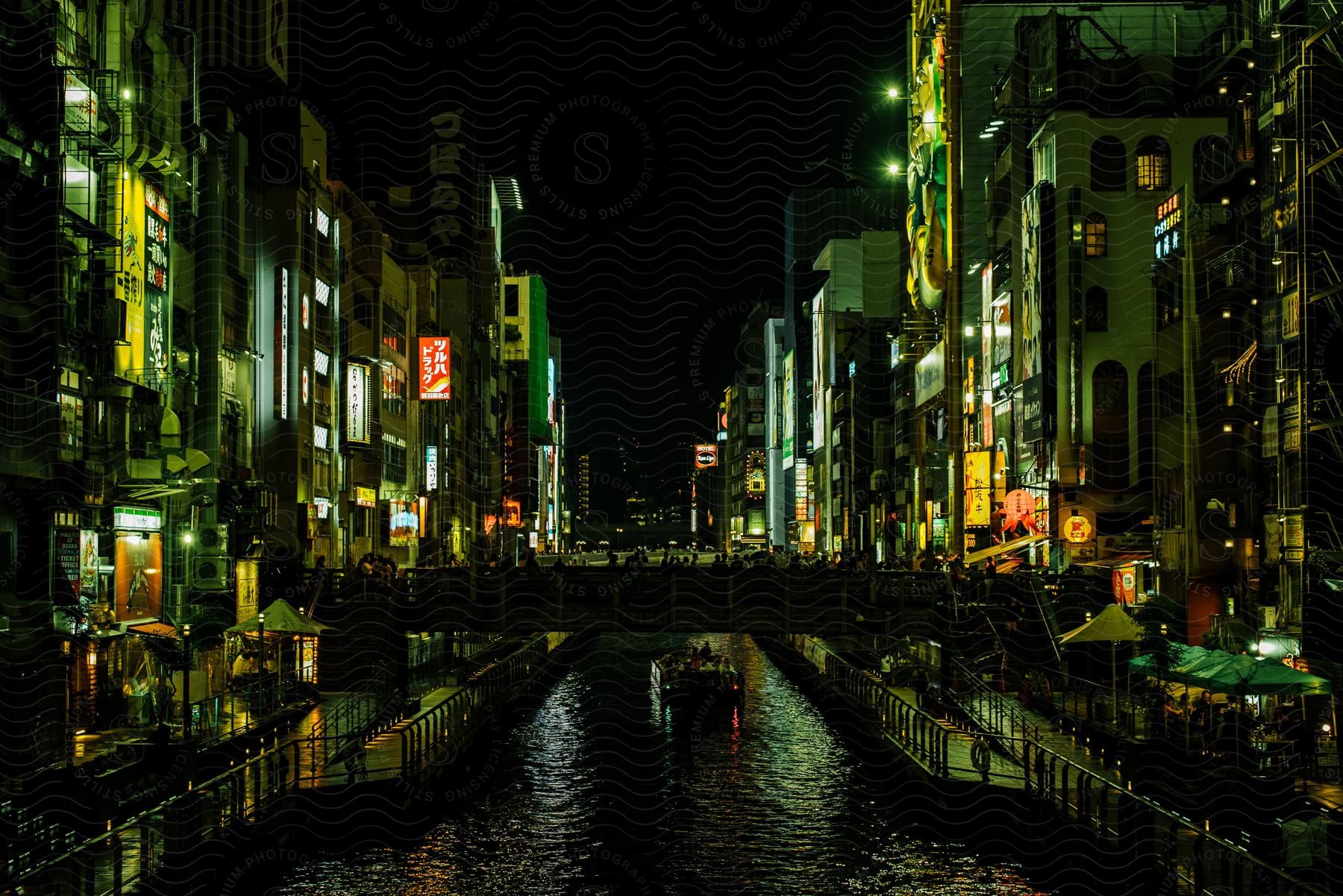 A neon-lit Osaka Dōtonbori river cruise at night, with people-filled boats navigating the waters between illuminated buildings on both sides.