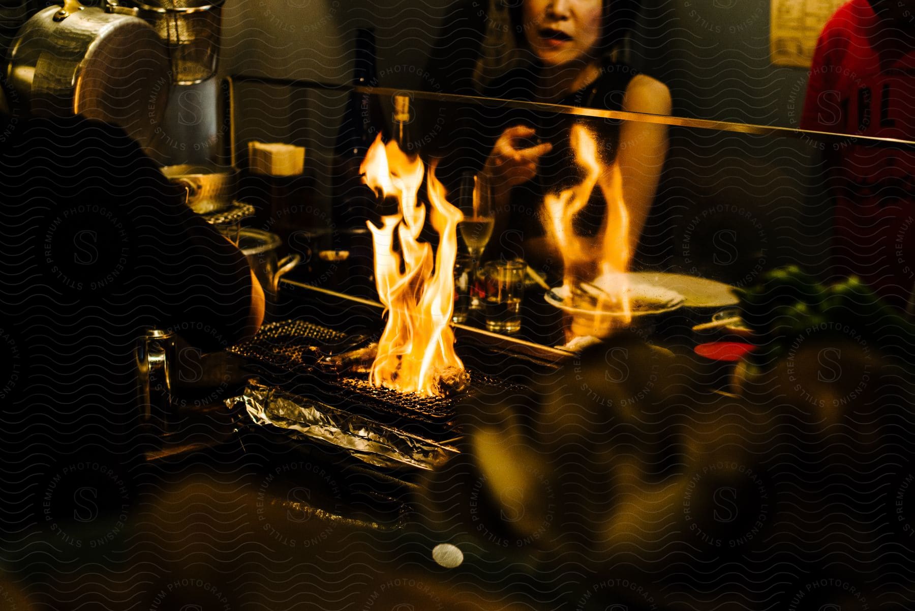 A Woman Watches A Meal Being Cooked Over An Open Flame In A Restaurant