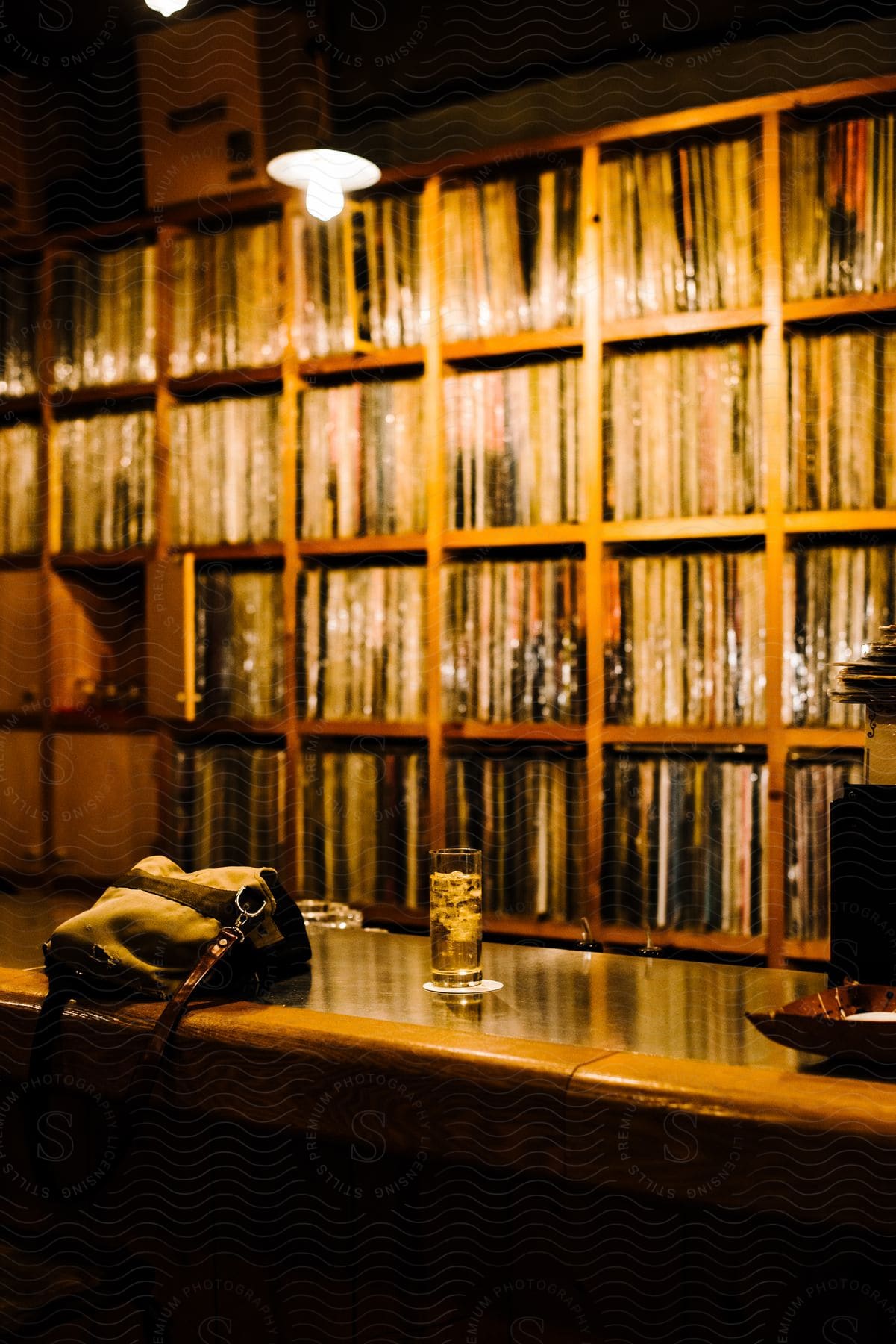 A single beverage in a glass sits atop a counter with shelves full of books behind it.