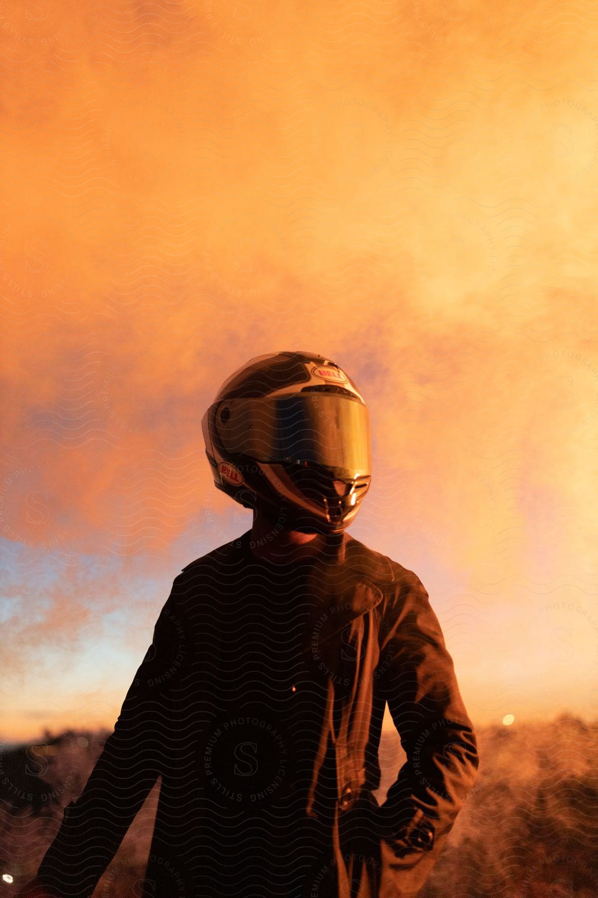 a person wearing a jacket and a full face covering helmet standing in an area with short grasses