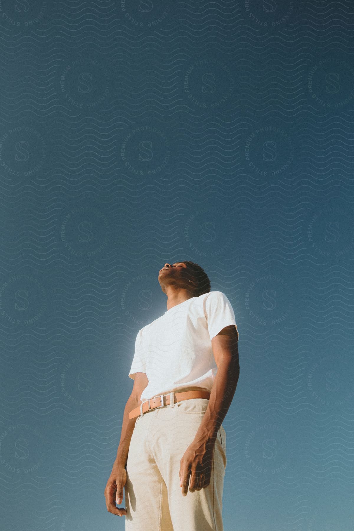 A black man stands in light colored clothing.