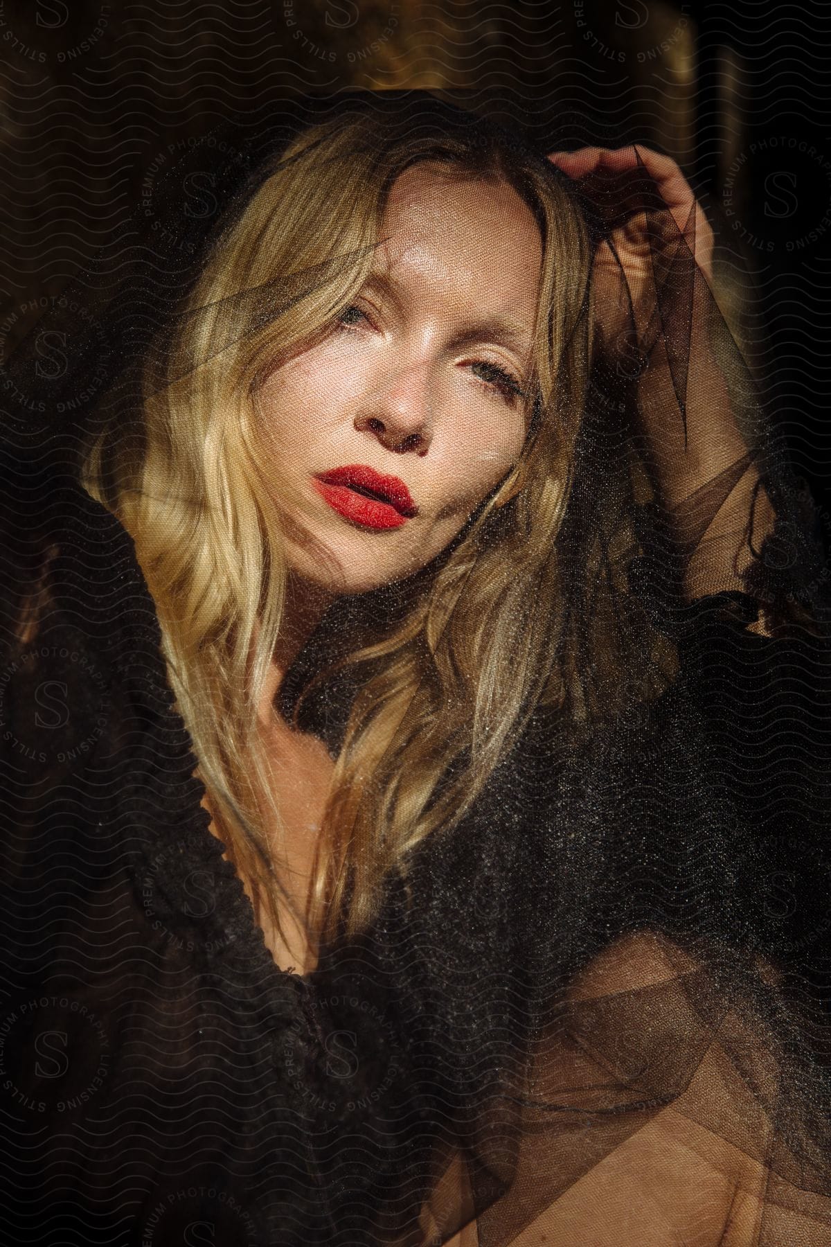 Light shines on the face of a blonde haired woman wearing red lipstick and a black laced dress