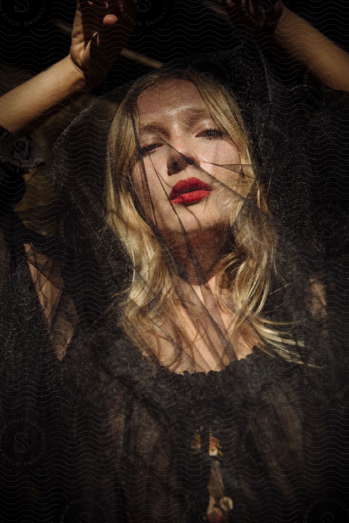 A blonde woman wearing red lipstick poses with her arms raised above her head.