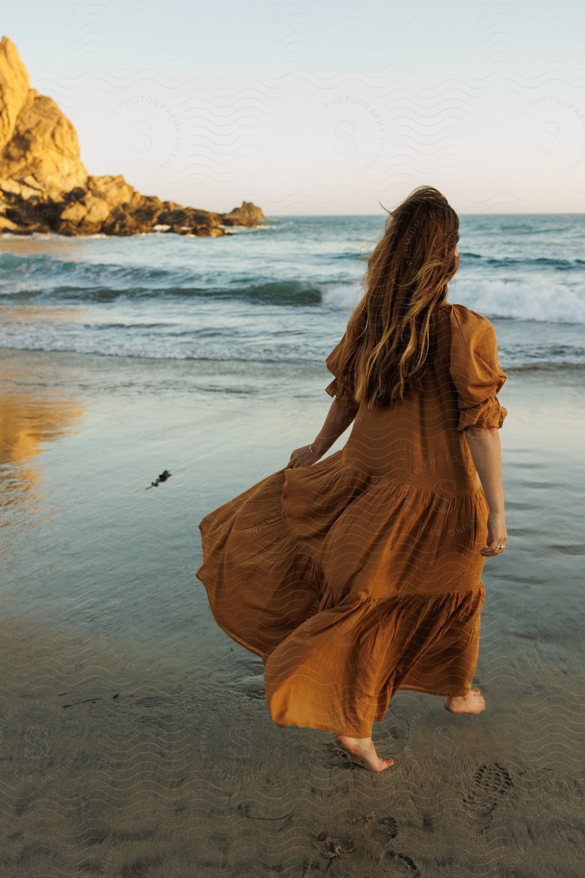 A barefoot woman in flowing brown dress on a sandy beach.