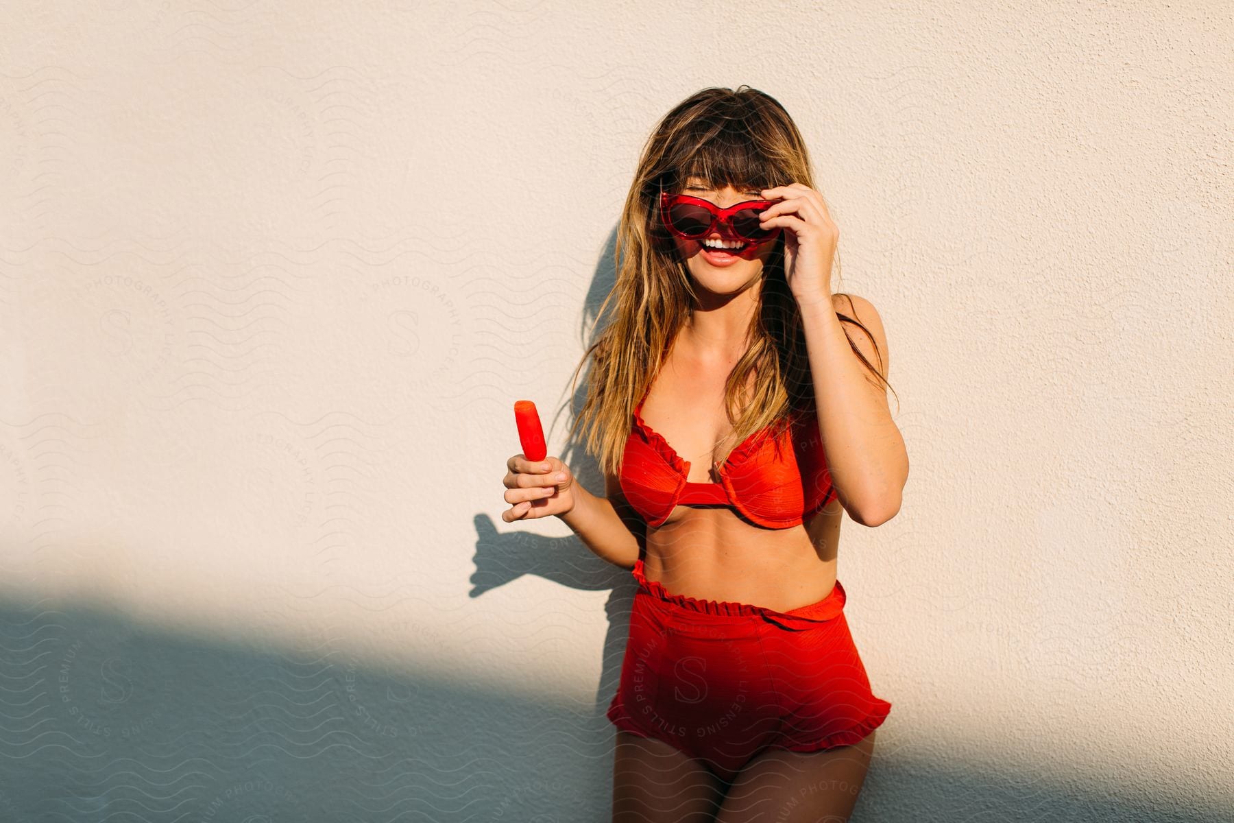 Woman smiles while wearing a bikini that matches the color of her popsicle.