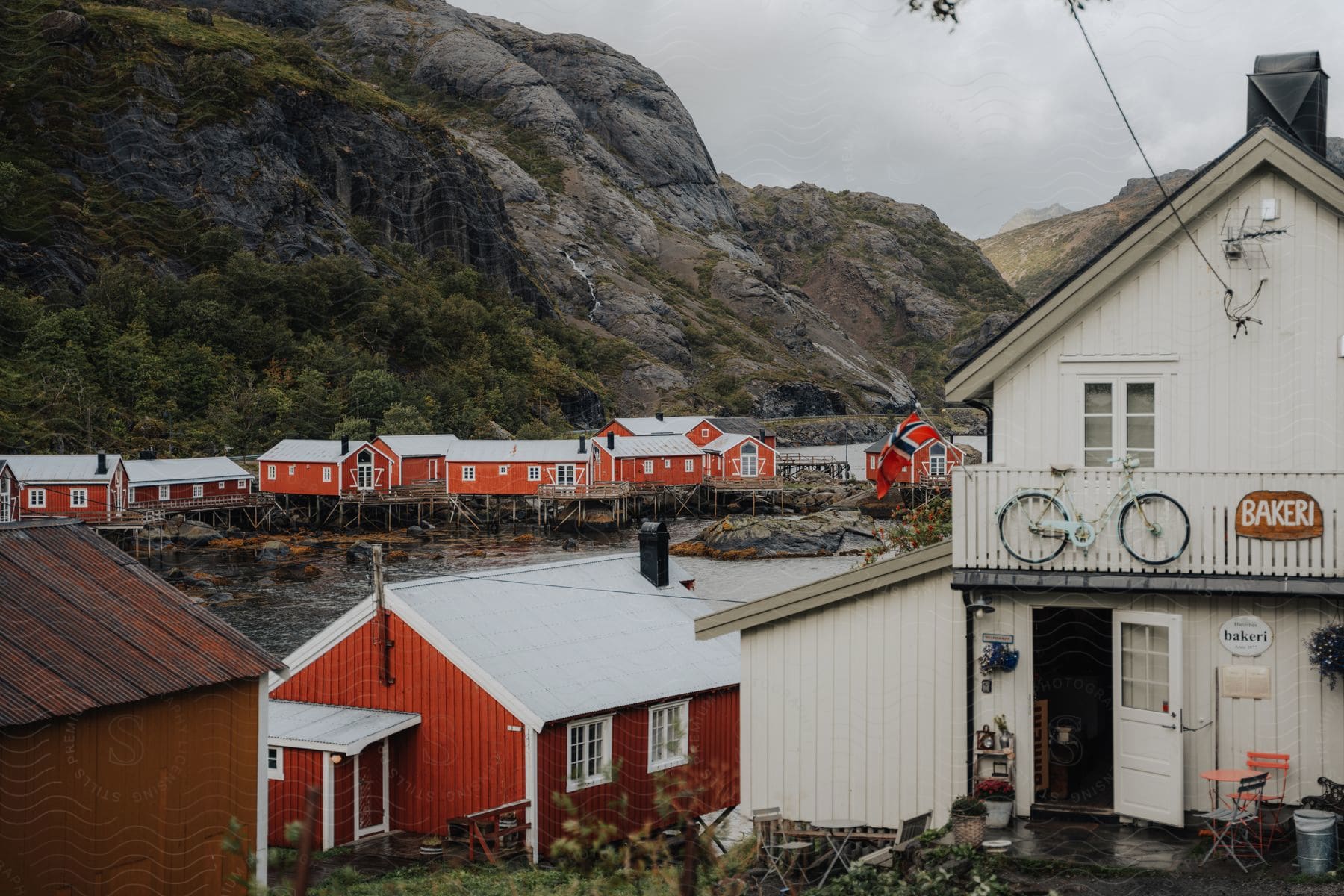 A red town on stilts huddled under a cloudy sky, with a white boat and a bike on its balcony, in the Lofoten Islands.