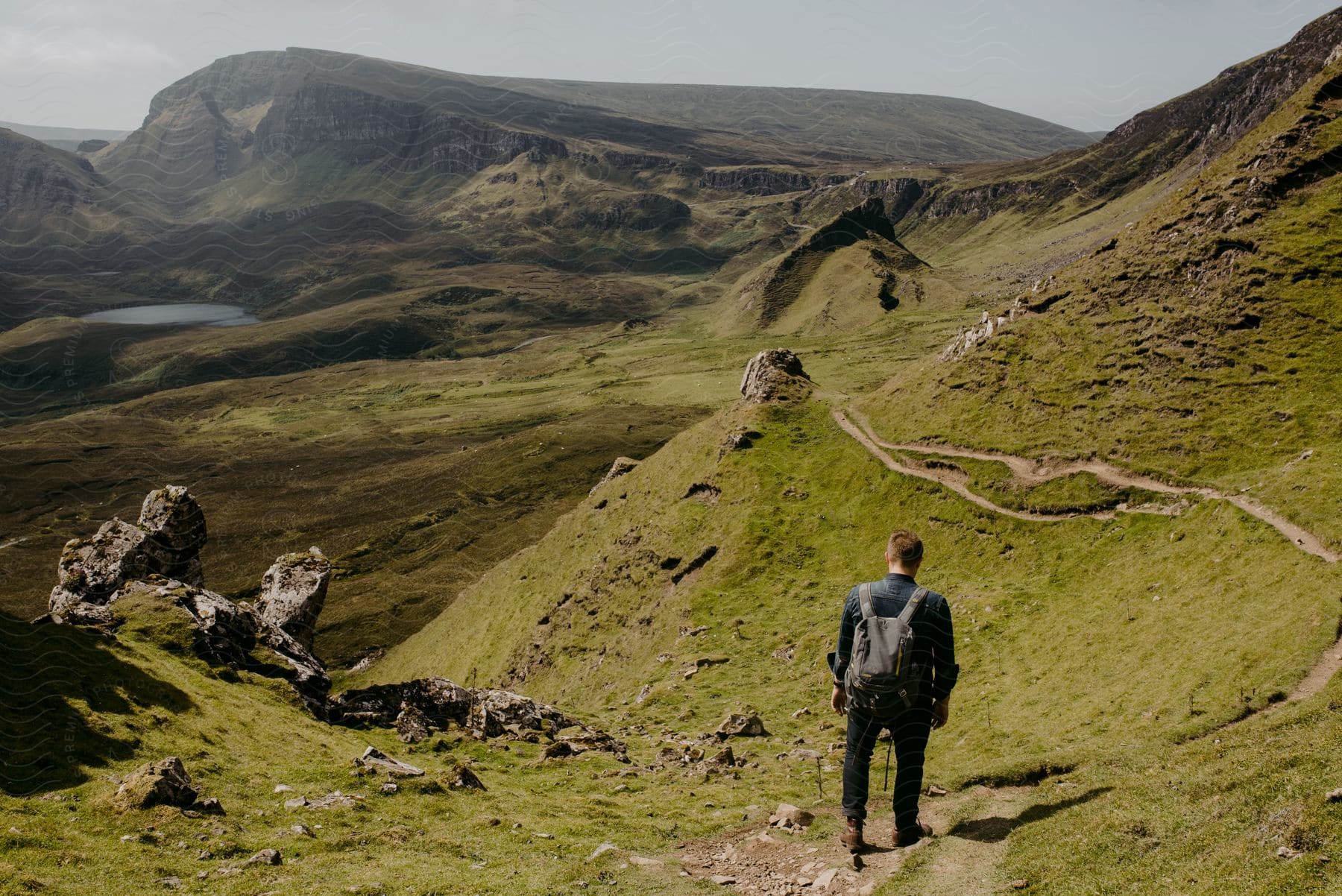 A hiker walks along a path cut into the side of a grassy hill.