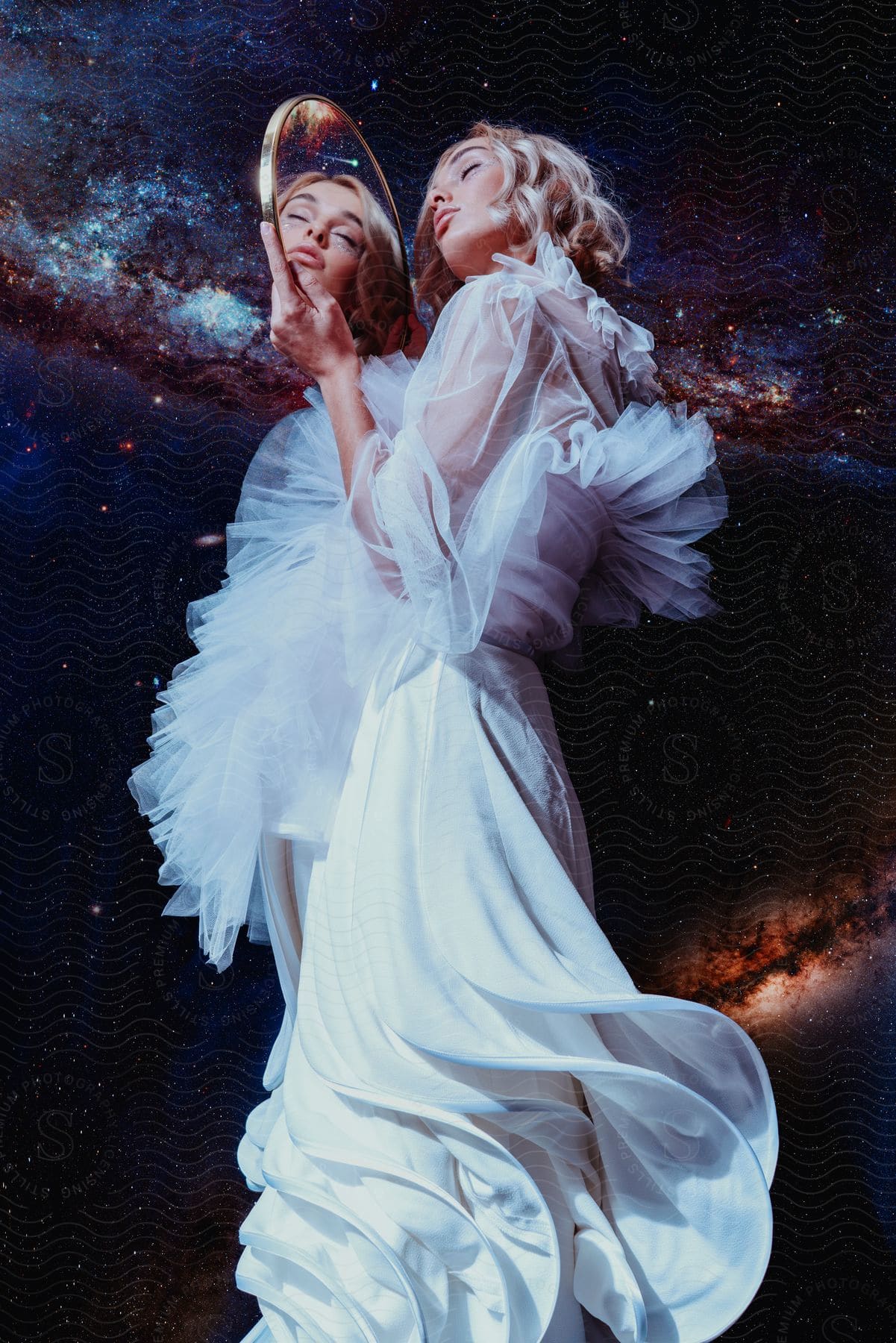 Woman wearing white dress holds mirror reflecting her face and the surrounding outer space.