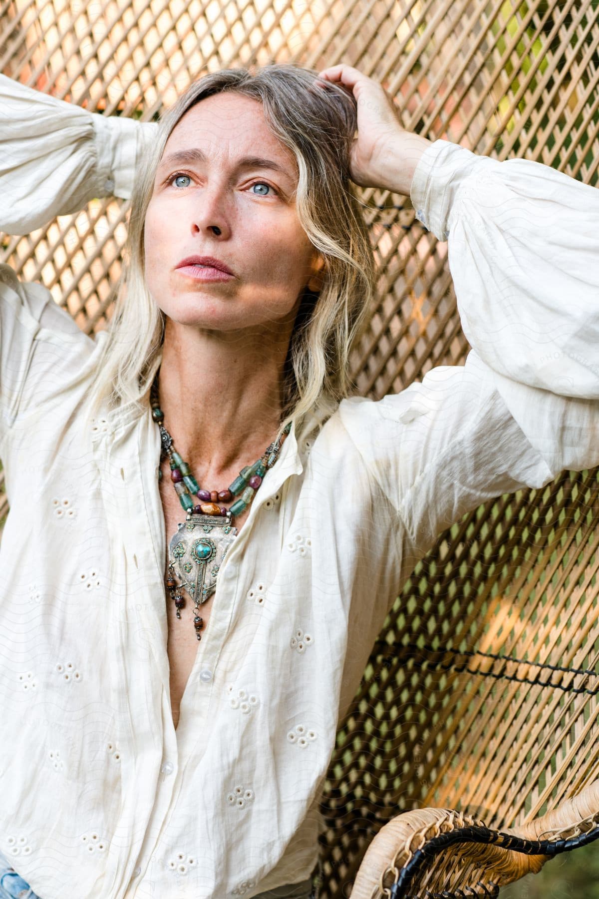 Woman with gray hair and light blue pendant, a white shirt, and jeans, sits in a chair in the yard.