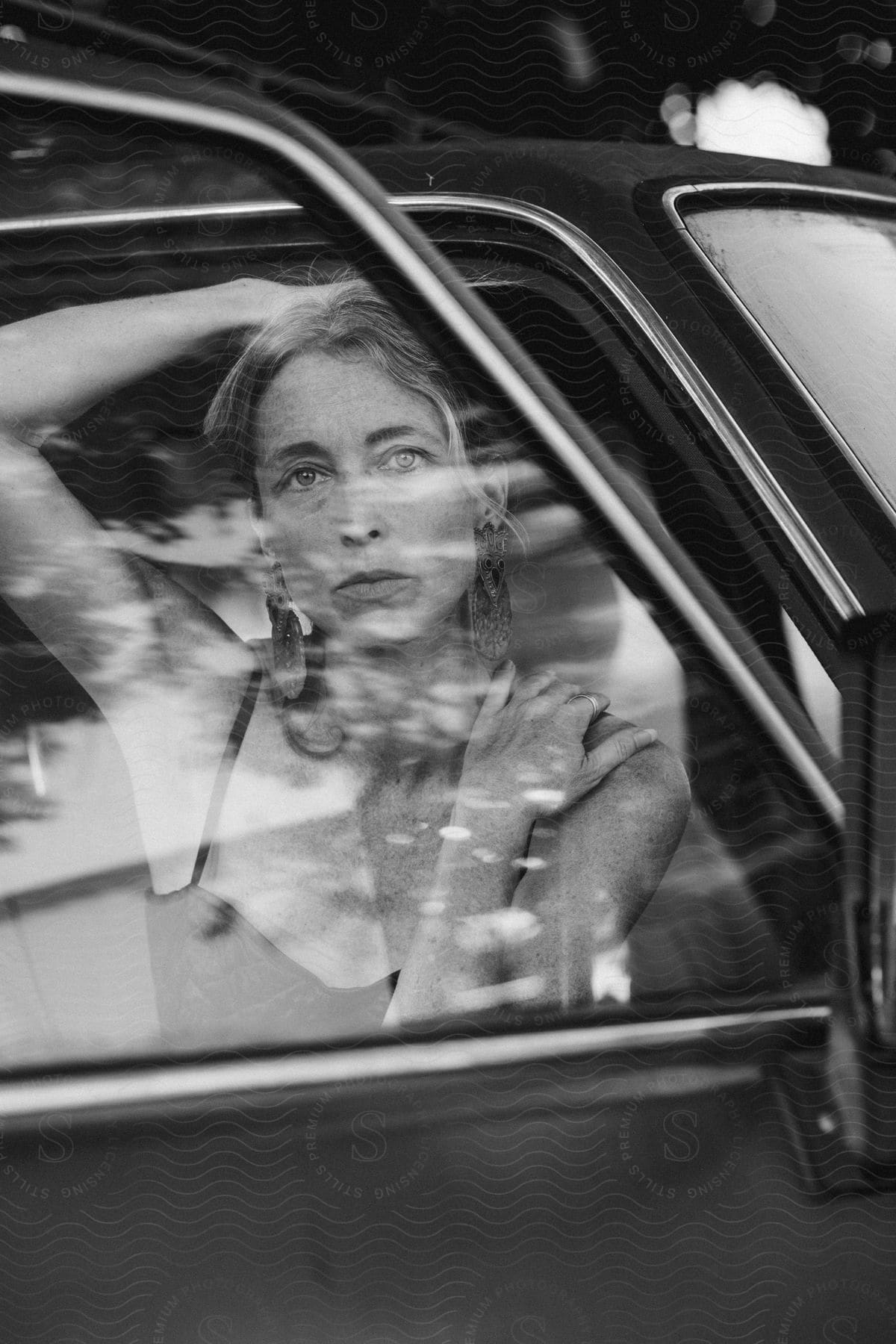 A woman poses provocatively behind a rolled-up car window, one hand on her head and the other on her shoulder.