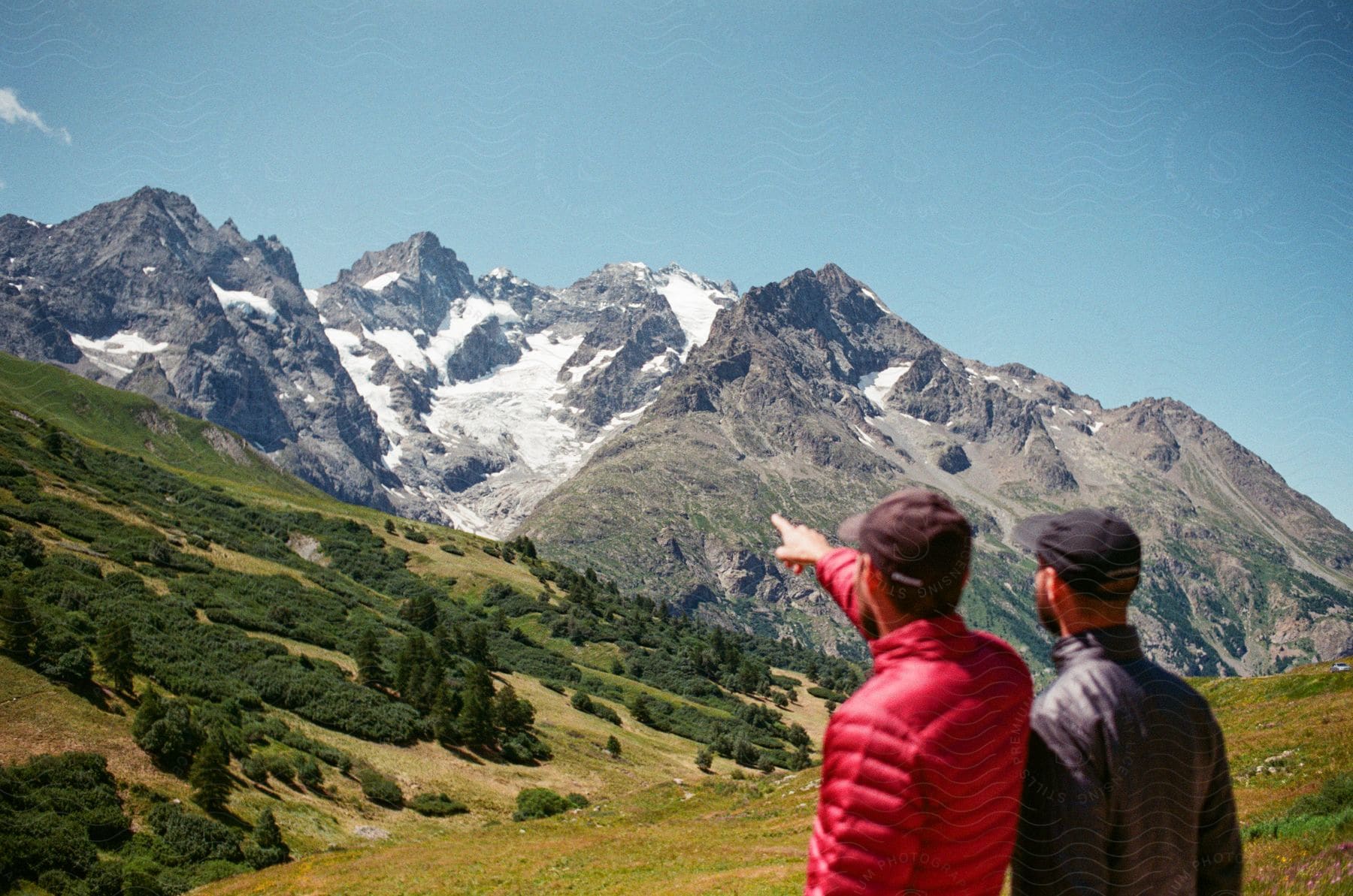 Two people looking at a massive mountain range , one of them pointing to the summit.