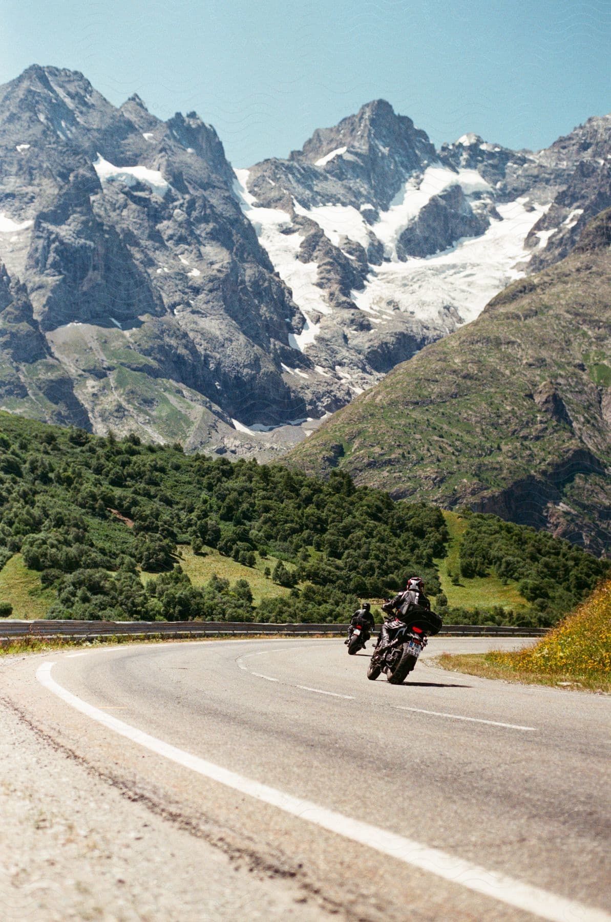 Two motorcyclists are riding on the road through the mountains.