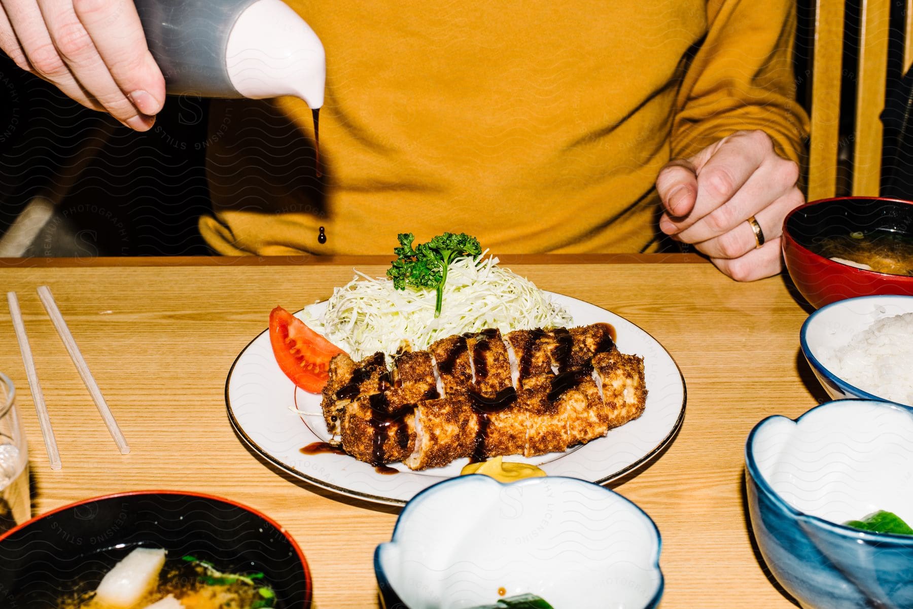 Woman flavors meat on dish with sauce while sitting at table.