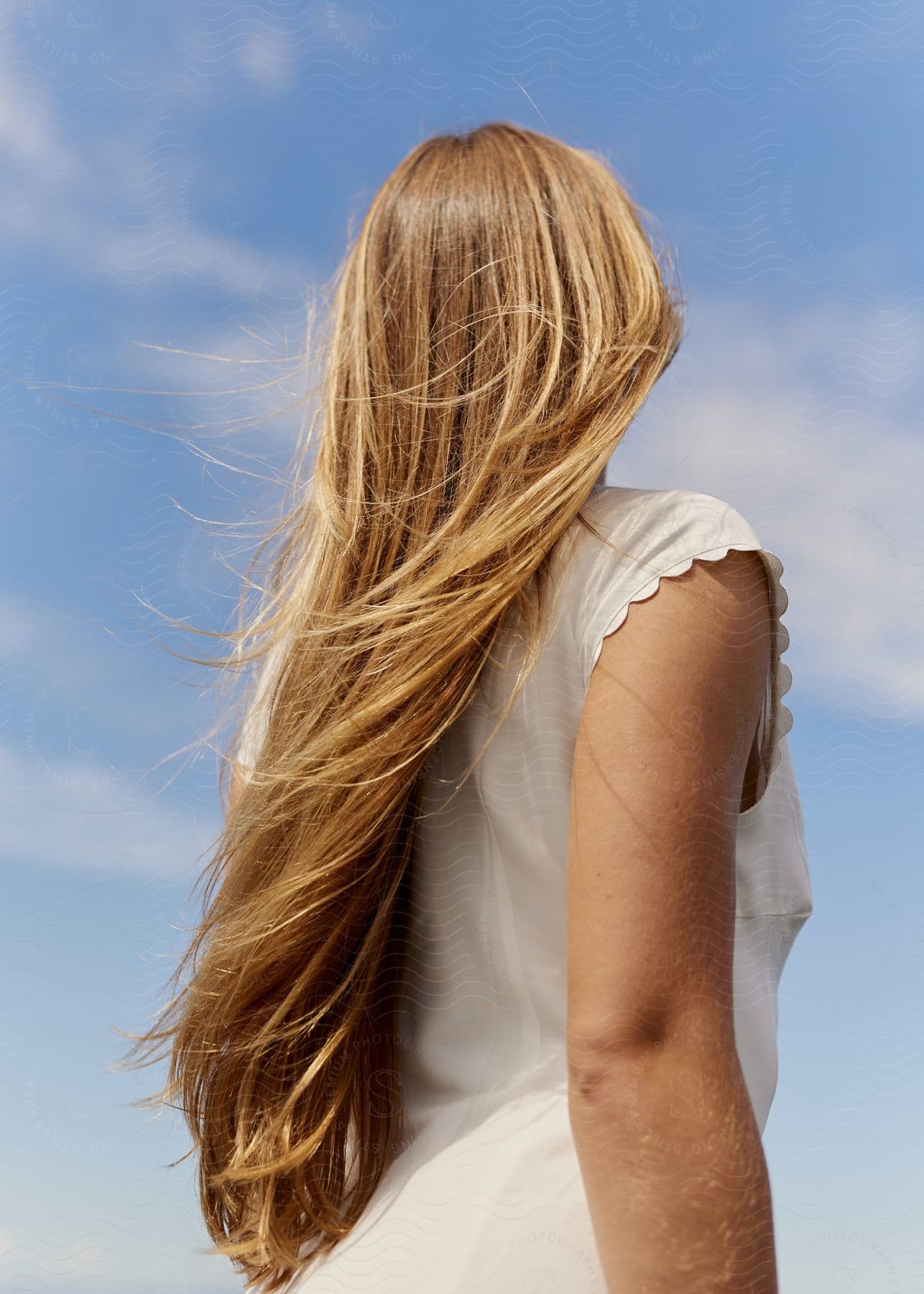 Blonde woman with long hair wearing white gazing at the sunny blue sky