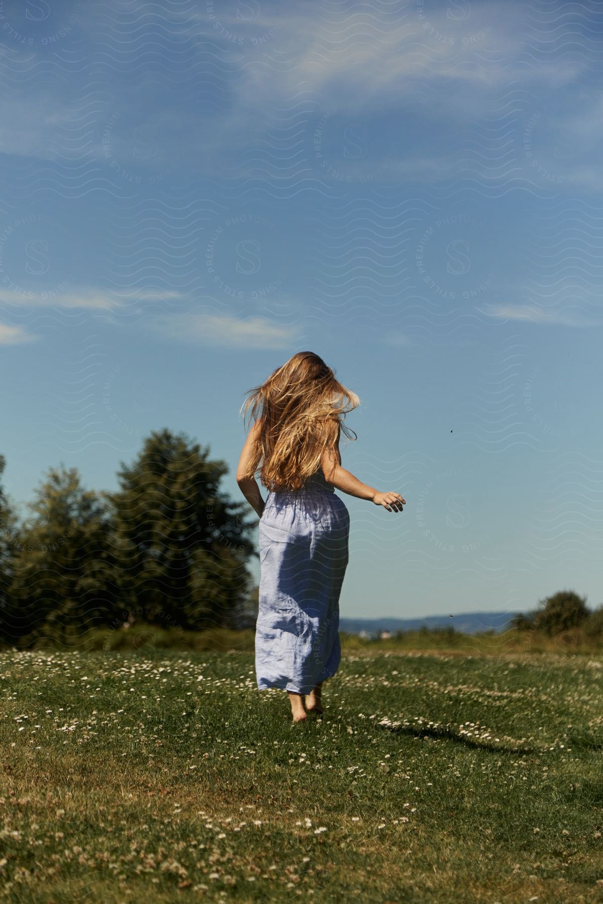 A woman running barefoot in the grass with long blonde hair cascading down her back