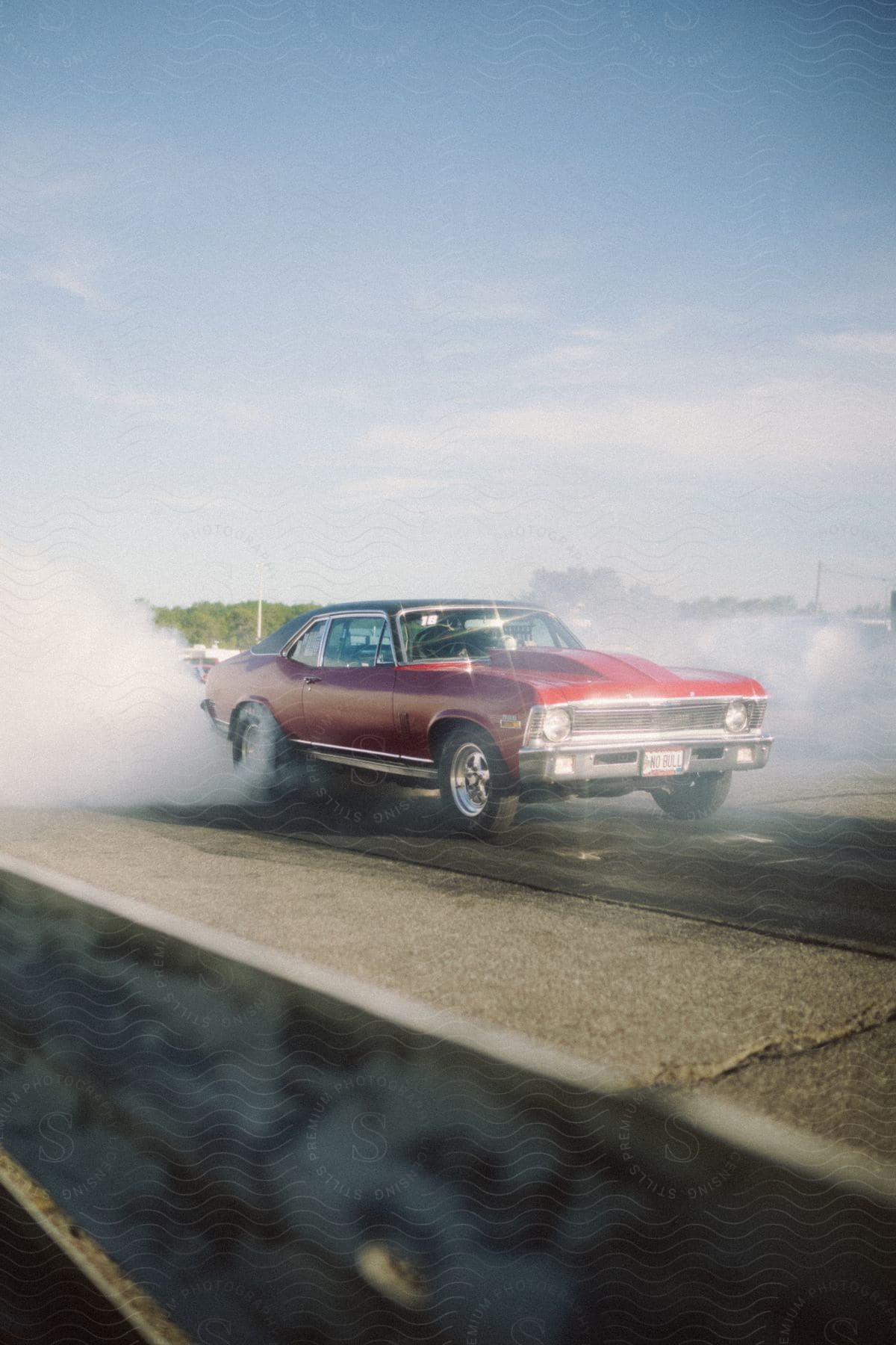 A candy apple red Chevy Nova burns out on a drag strip, spewing smoke from its rear tires.