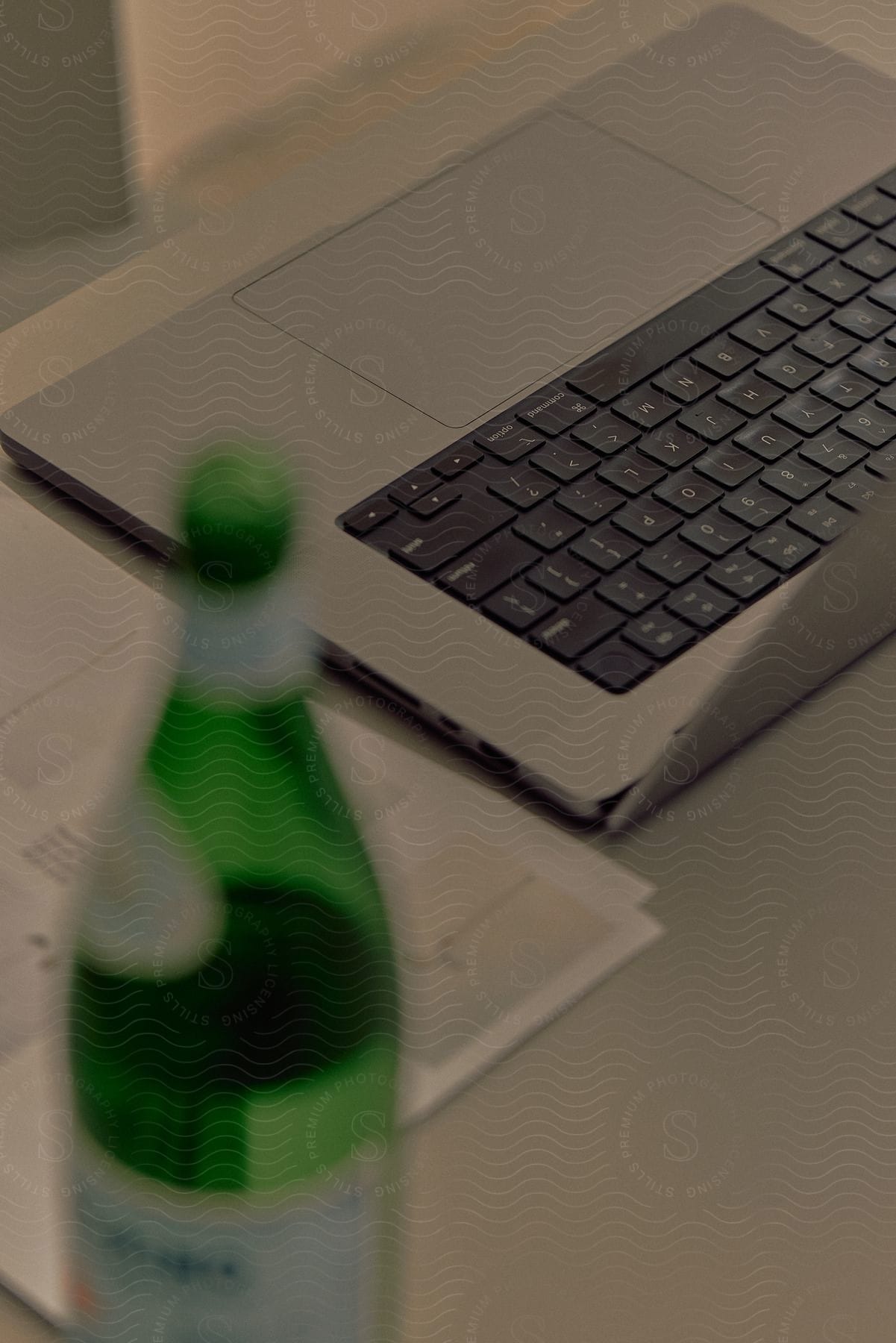Laptop on a desk with a green glass bottle next to it.