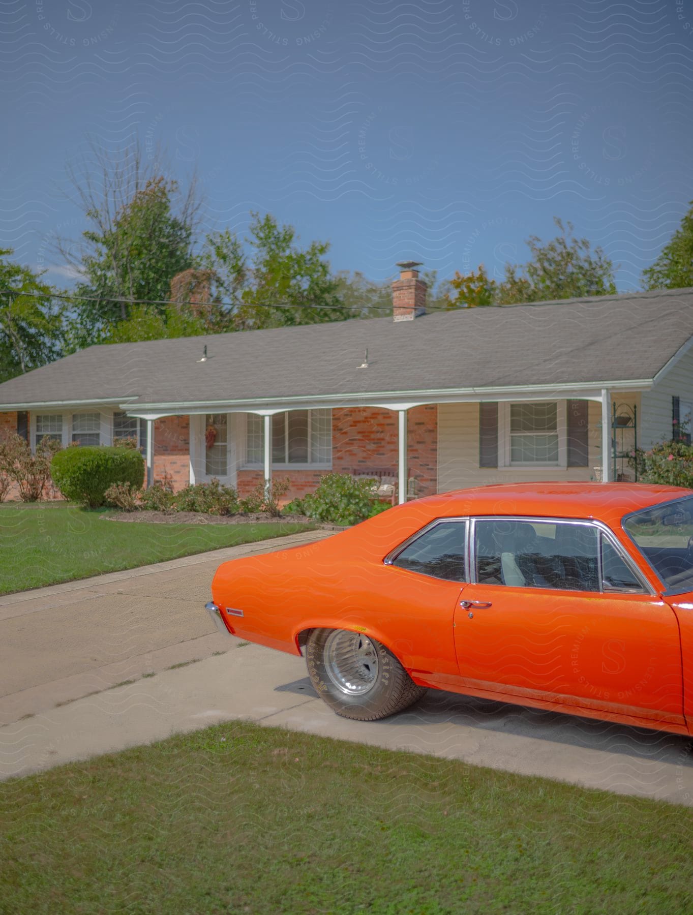 A bright orange Chevy Nova gleams on the driveway of a suburban home.