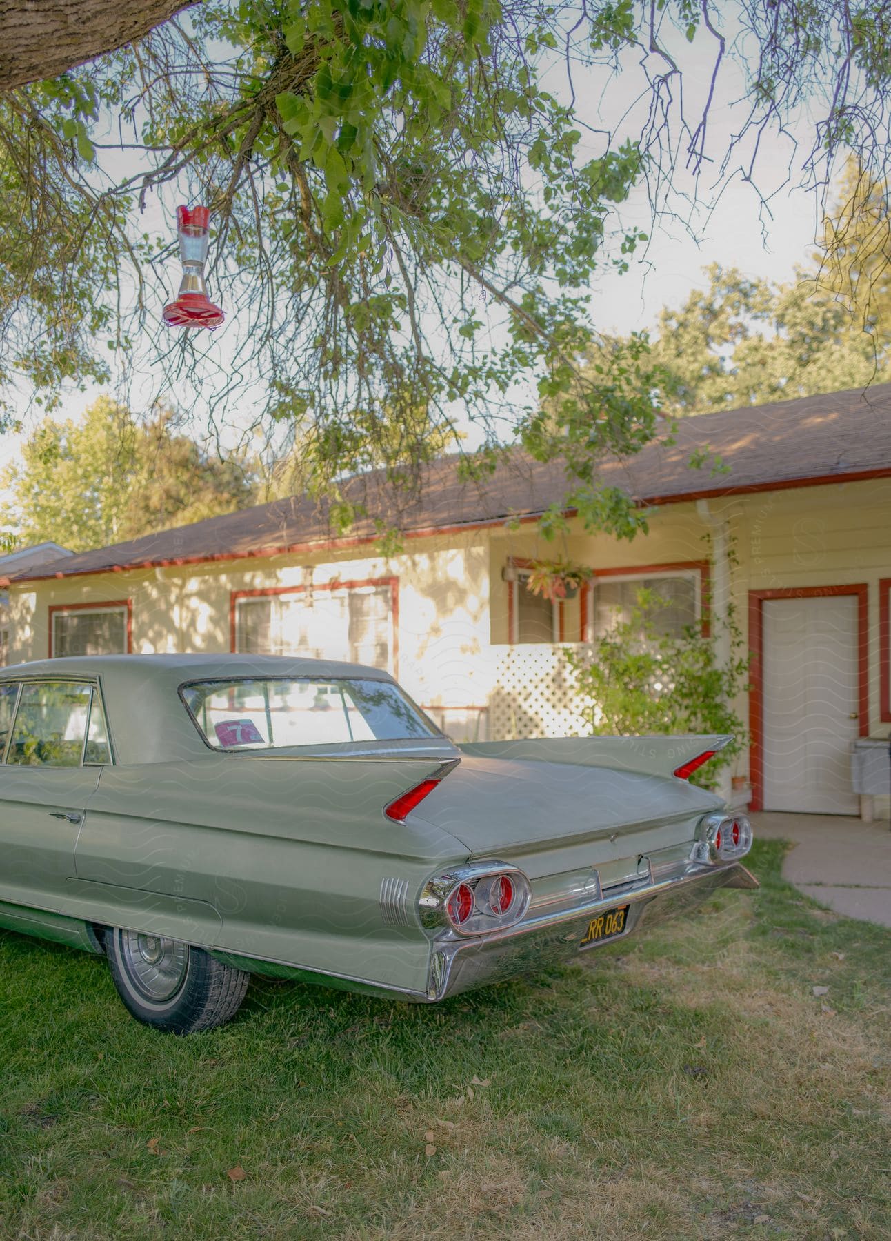 A classic 1960s Cadillac deVille Town Sedan rests under a shady tree, its bird feeder swaying gently in the breeze.