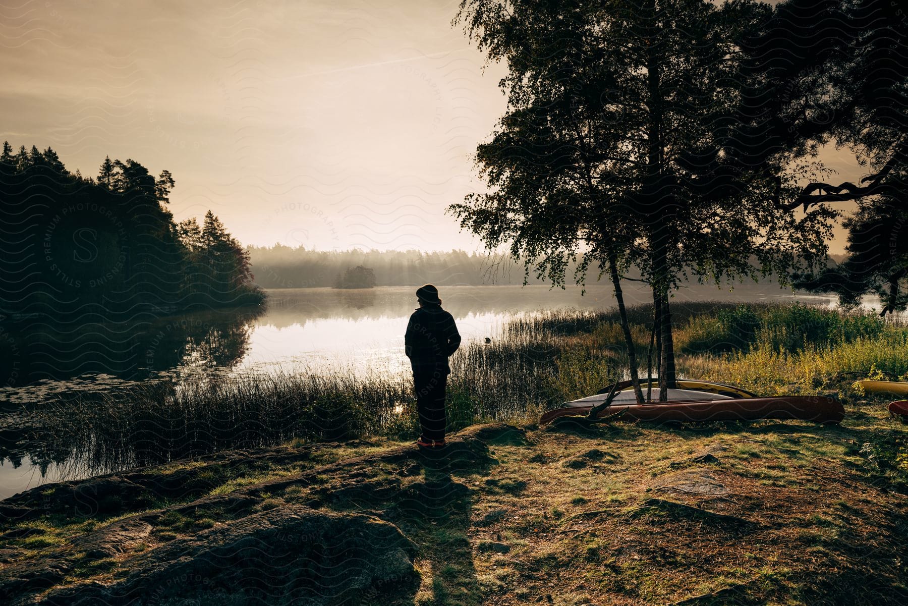 A man is standing looking into the pond as the sun is setting.