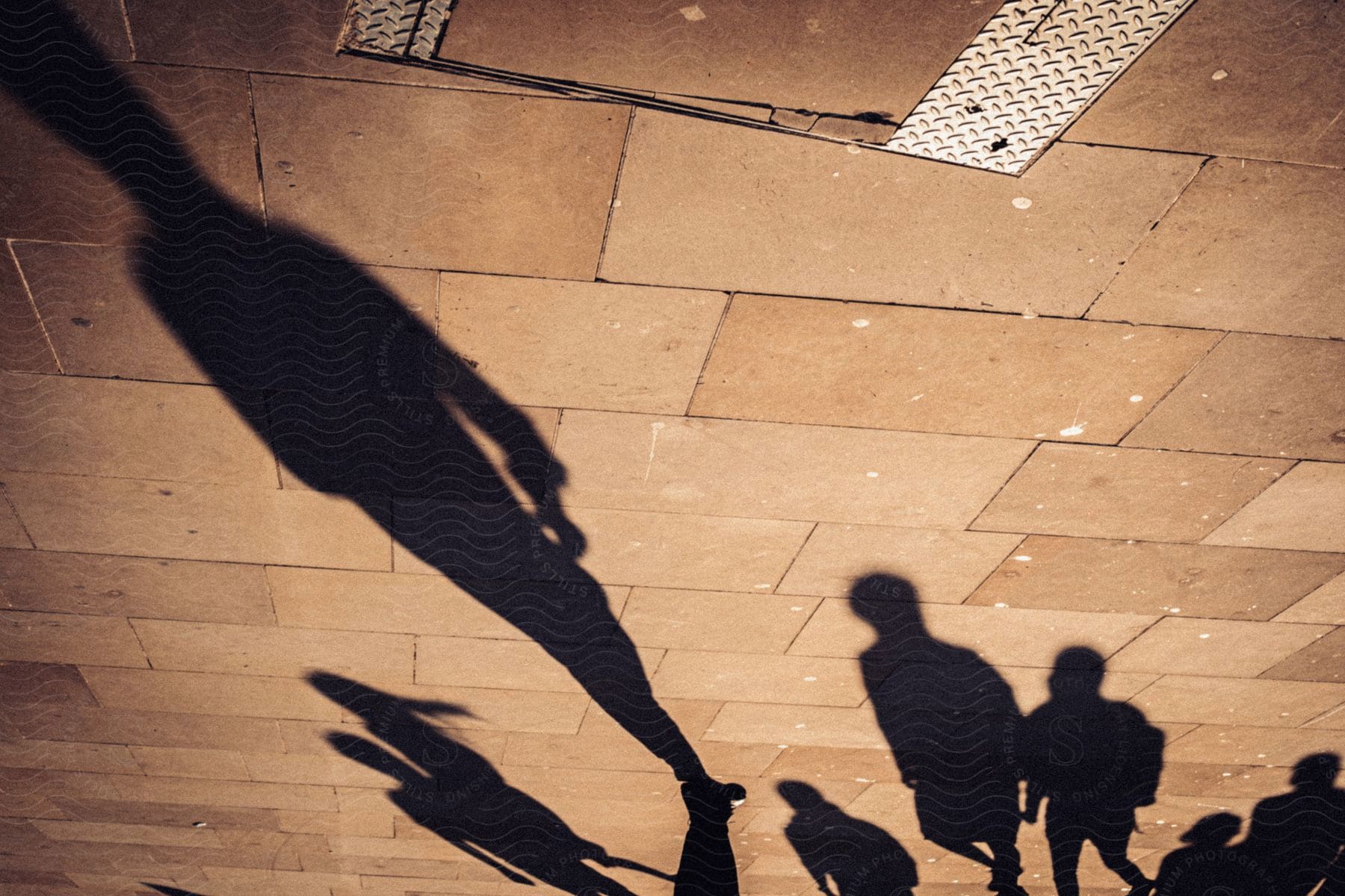 Elongated shadows on the pavement of people walking on the street.