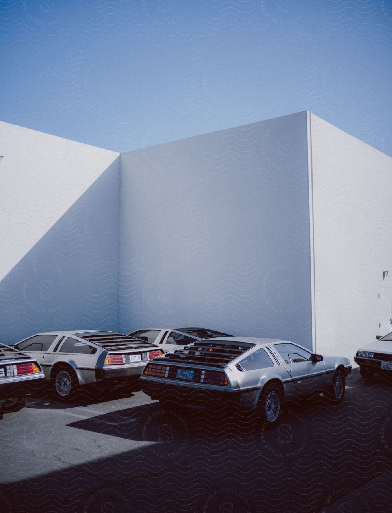 Several DeLorean cars parked in a lot near a white walled building on a sunny day