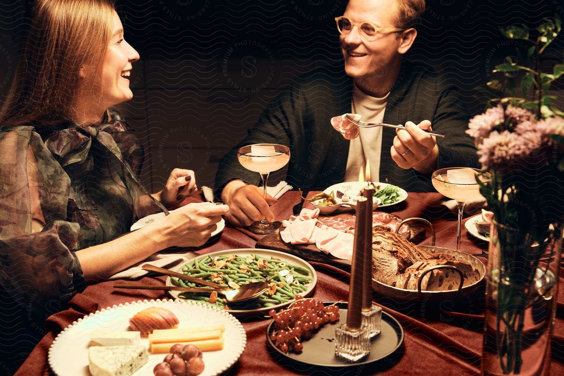 A couple sharing a meal of charcuterie and green beans with cocktails.