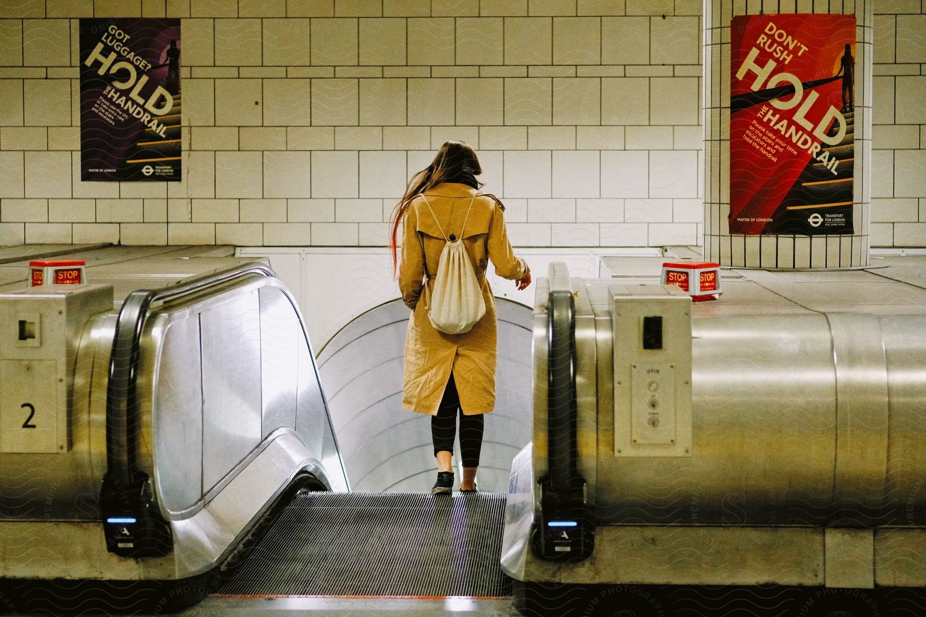 A woman wearing a coat and backpack getting on the escalator down to the subway