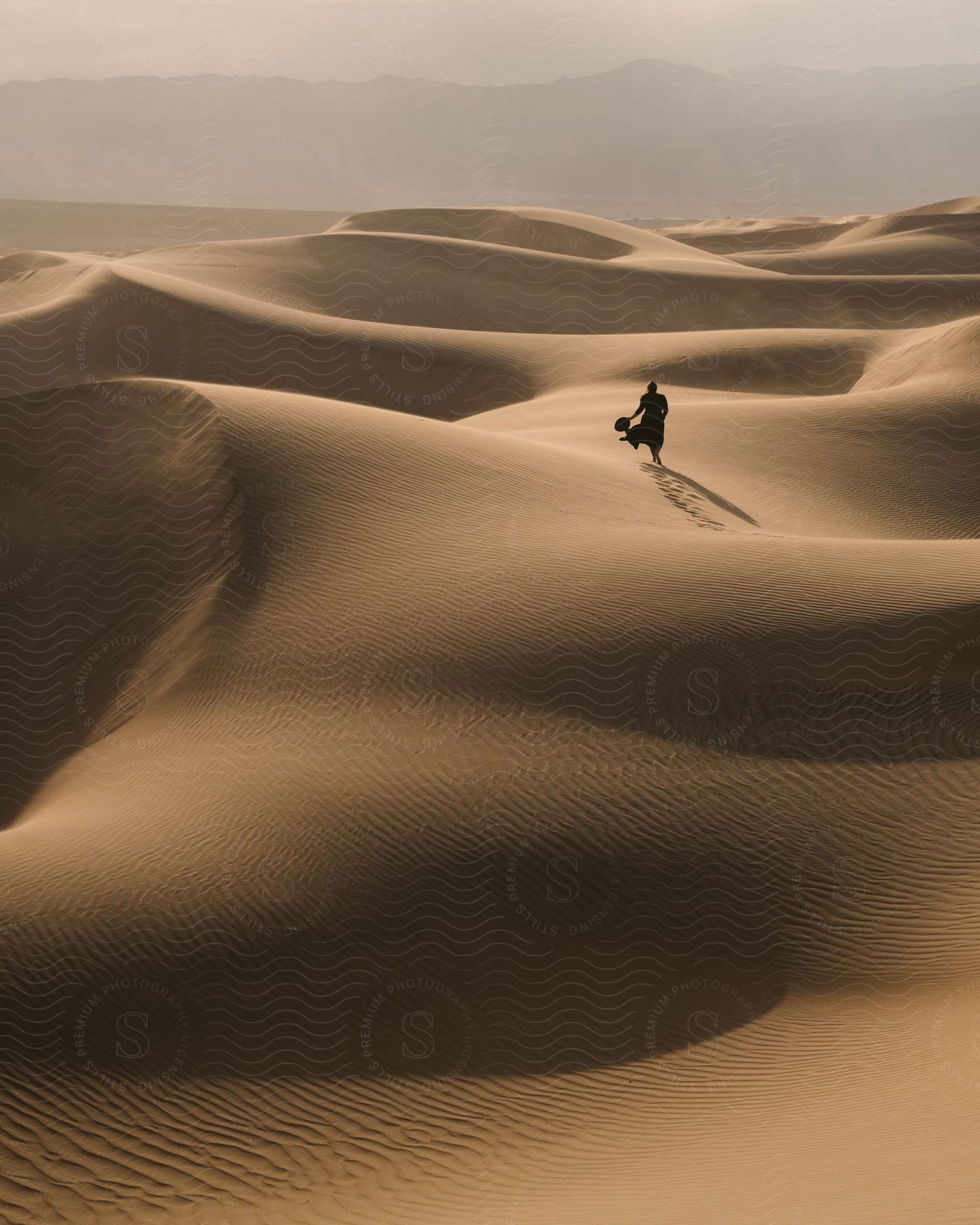 Silhouette of a person walking through the dunes in the desert.